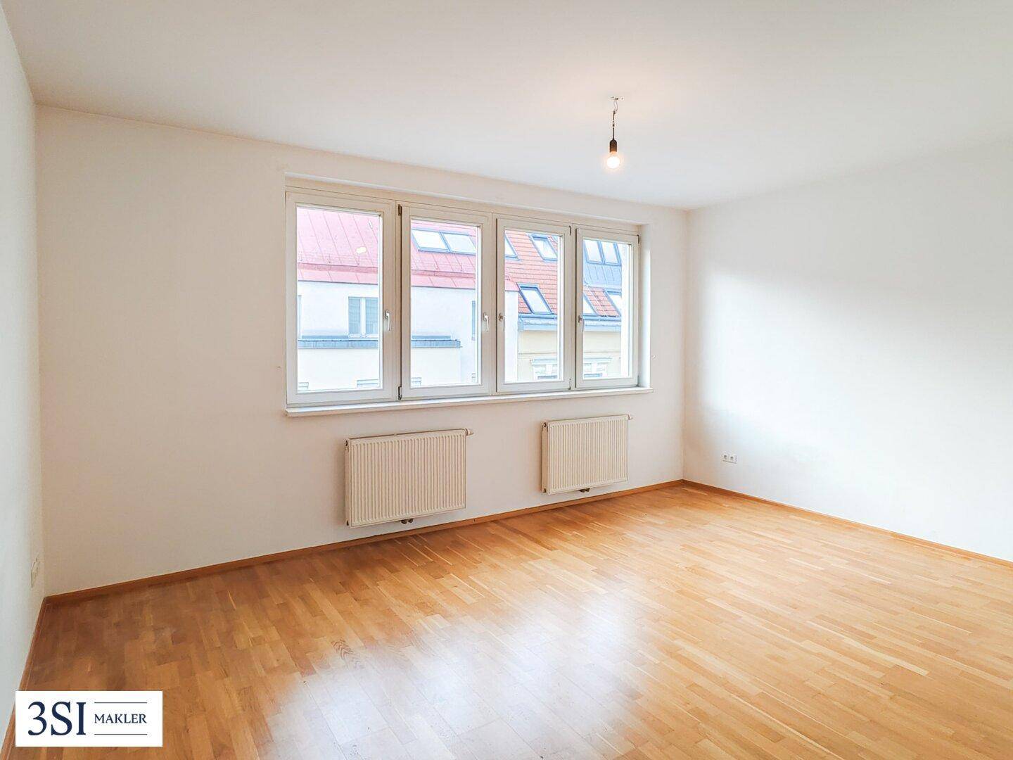 Helles Zimmer mit Parkettboden und großen Fenstern, ideal als Wohn- oder Schlafbereich.