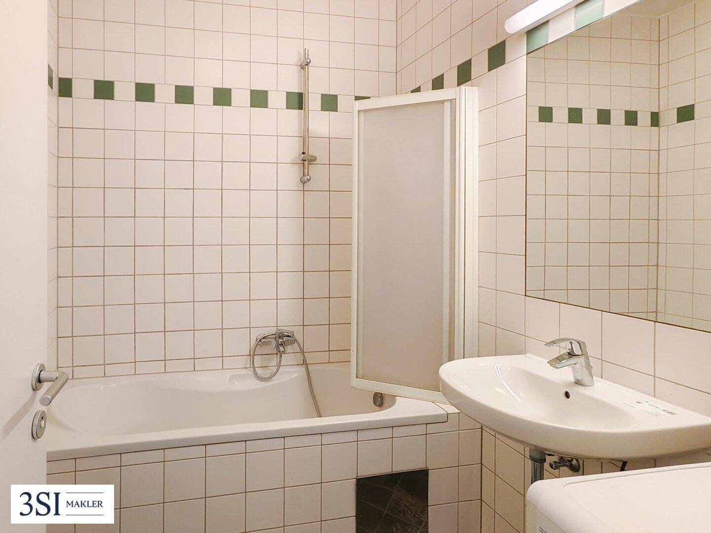 Badezimmer mit Badewanne, Waschbecken und weiß gefliesten Wänden mit grünen Akzenten.