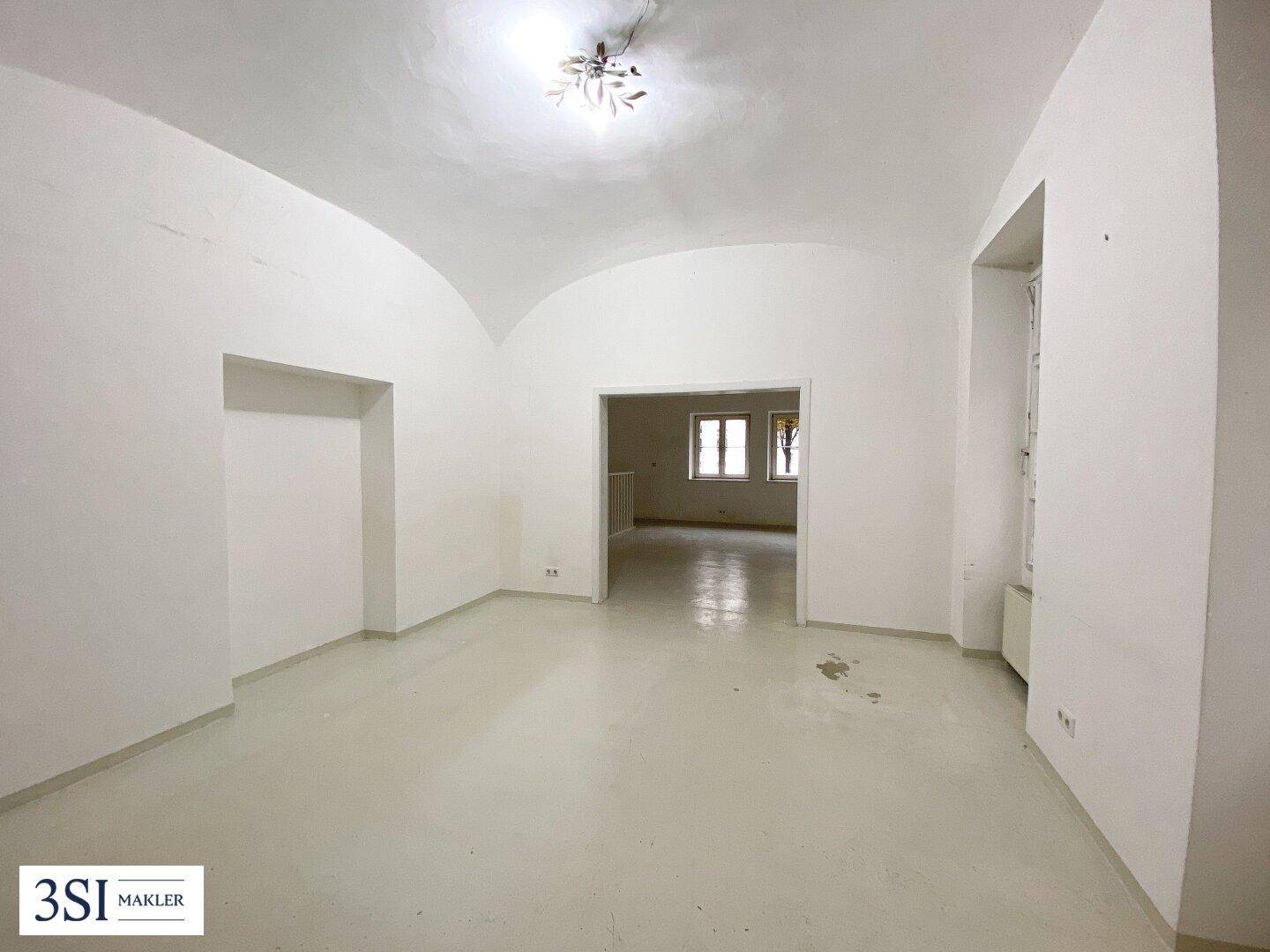 Großer, leerer Raum mit gewölbter Decke, hellen Wänden, einer Nische und einem Fenster.
