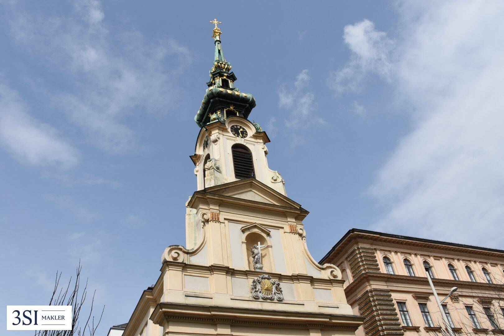Historischer Kirchturm mit barocken Elementen und einer Uhr unter blauem Himmel.