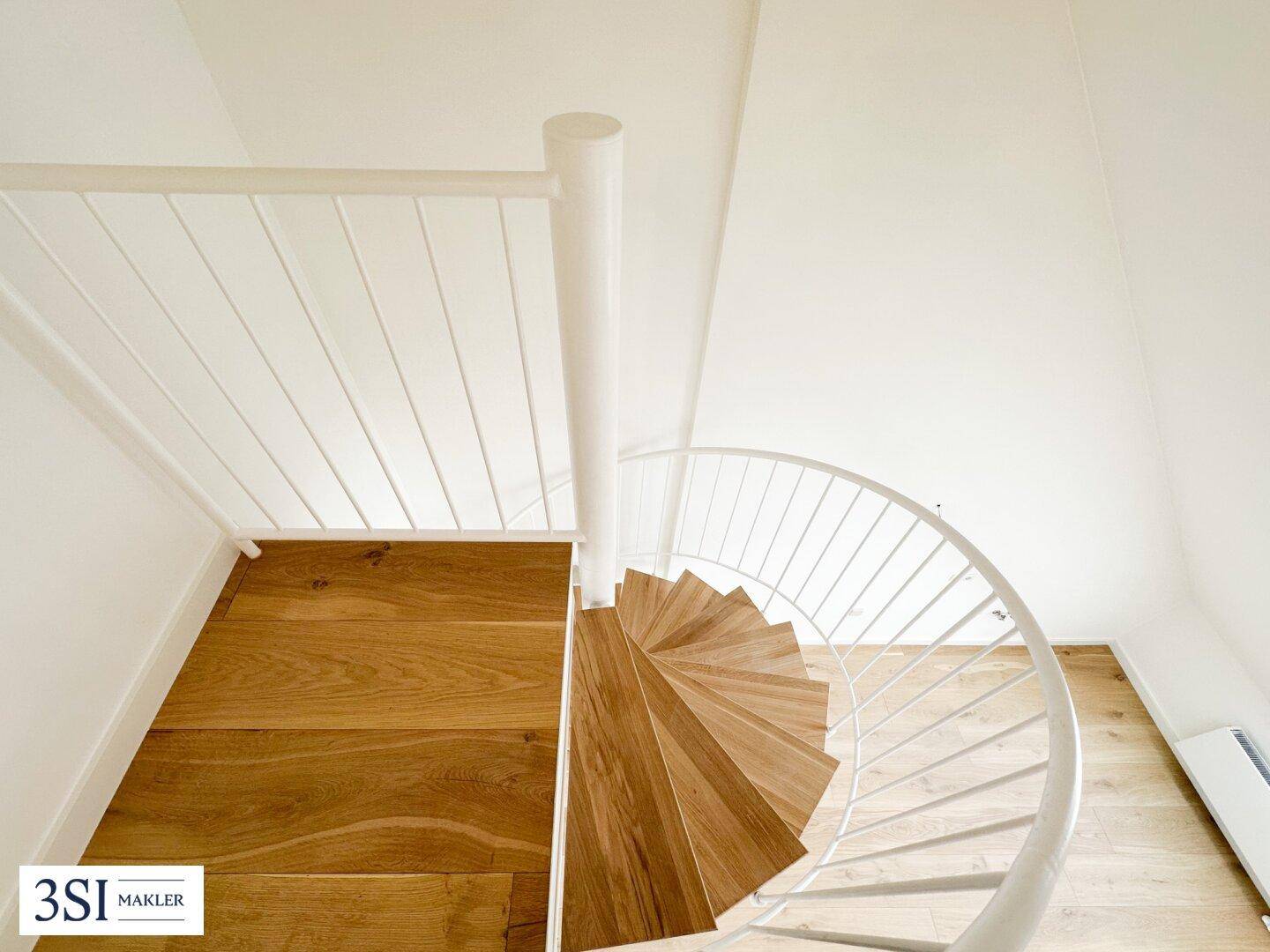 Elegante Wendeltreppe mit Holzstufen und weißem Geländer, die zwei Ebenen in einem Loft verbindet.