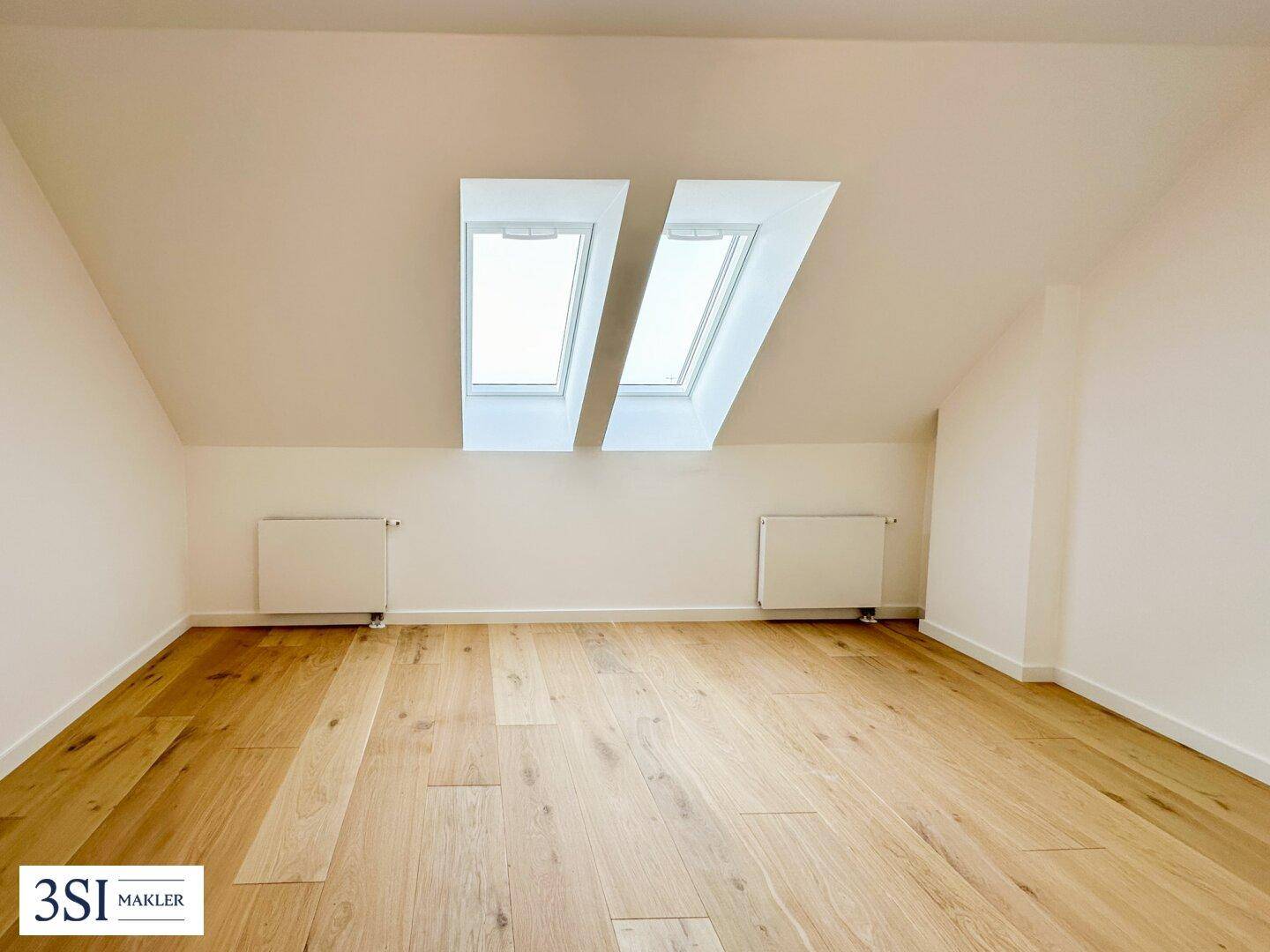 Helles Zimmer mit zwei Dachfenstern, Holzparkettboden und Dachschrägen, bietet viel Tageslicht.