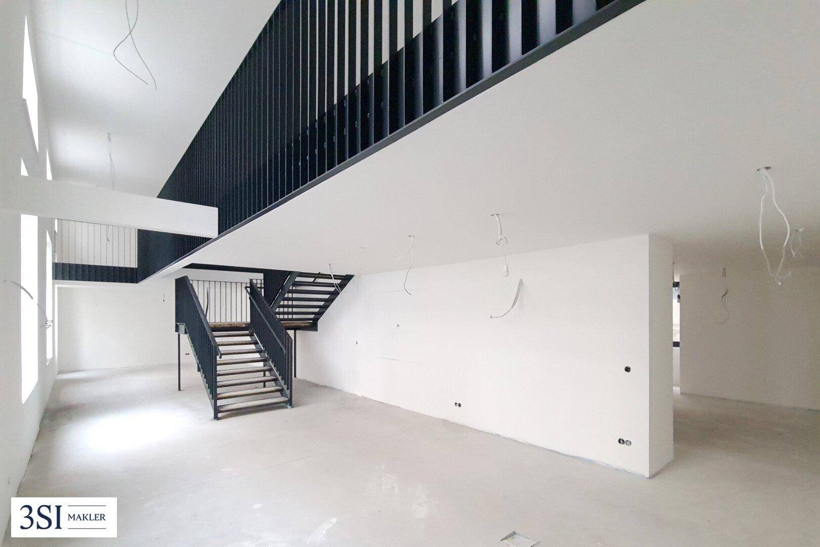 Heller, offener Raum im Rohbau mit moderner schwarzer Metalltreppe und hohen Decken.