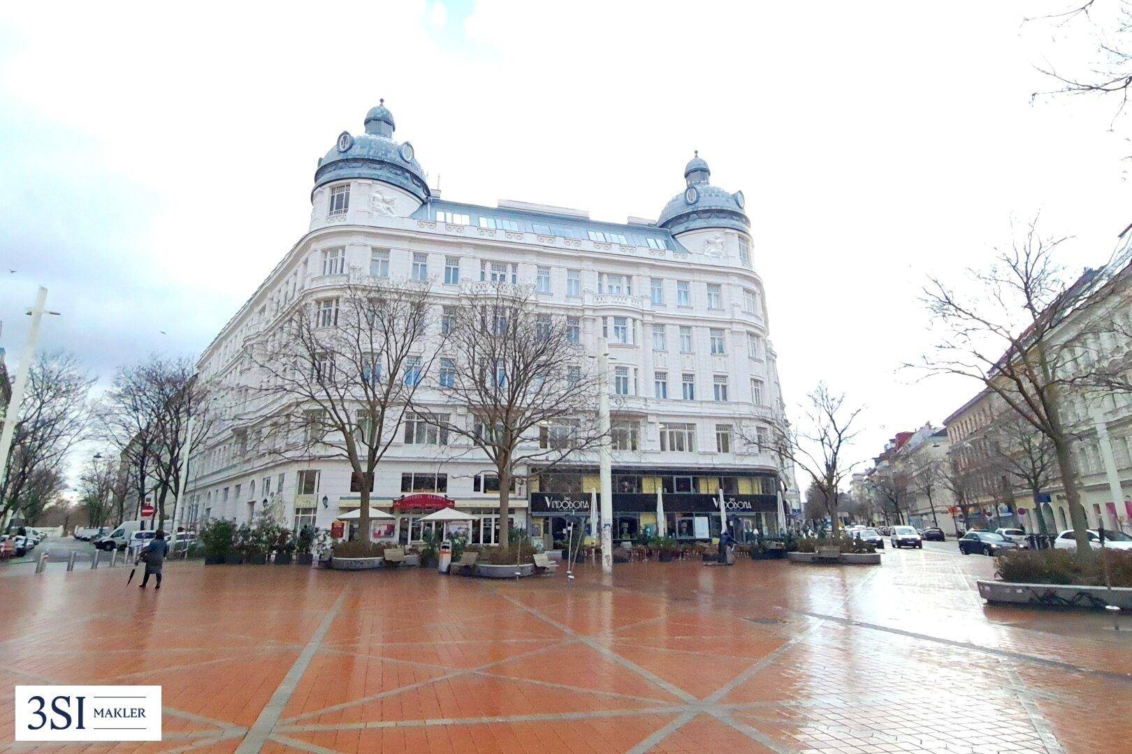 Historisches Gebäude mit markanter Architektur, Geschäften im Erdgeschoss und belebter Stadtansicht.