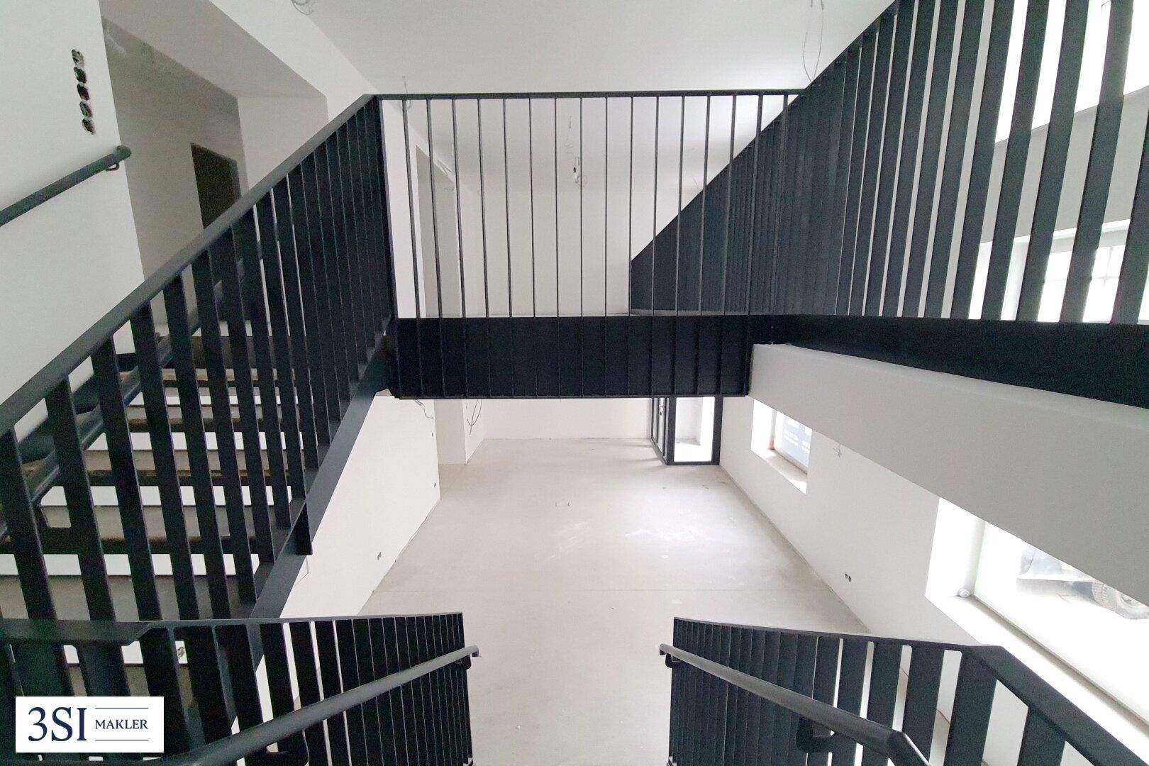 Blick von der modernen schwarzen Metalltreppe hinunter in den hellen, offenen Rohbauraum.