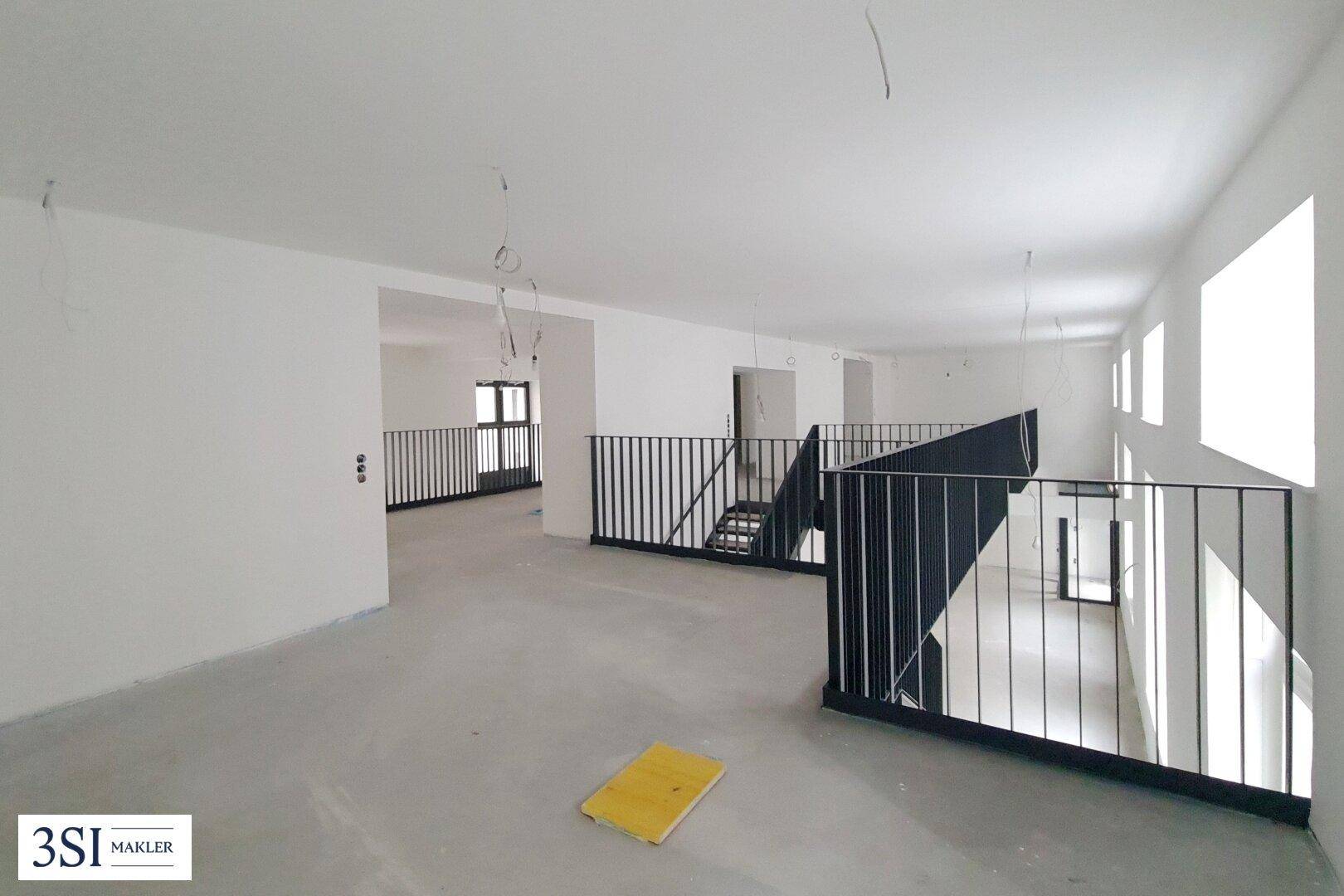 Obergeschoss eines offenen Rohbaus mit schwarzem Metallgeländer und Blick in den unteren Bereich.