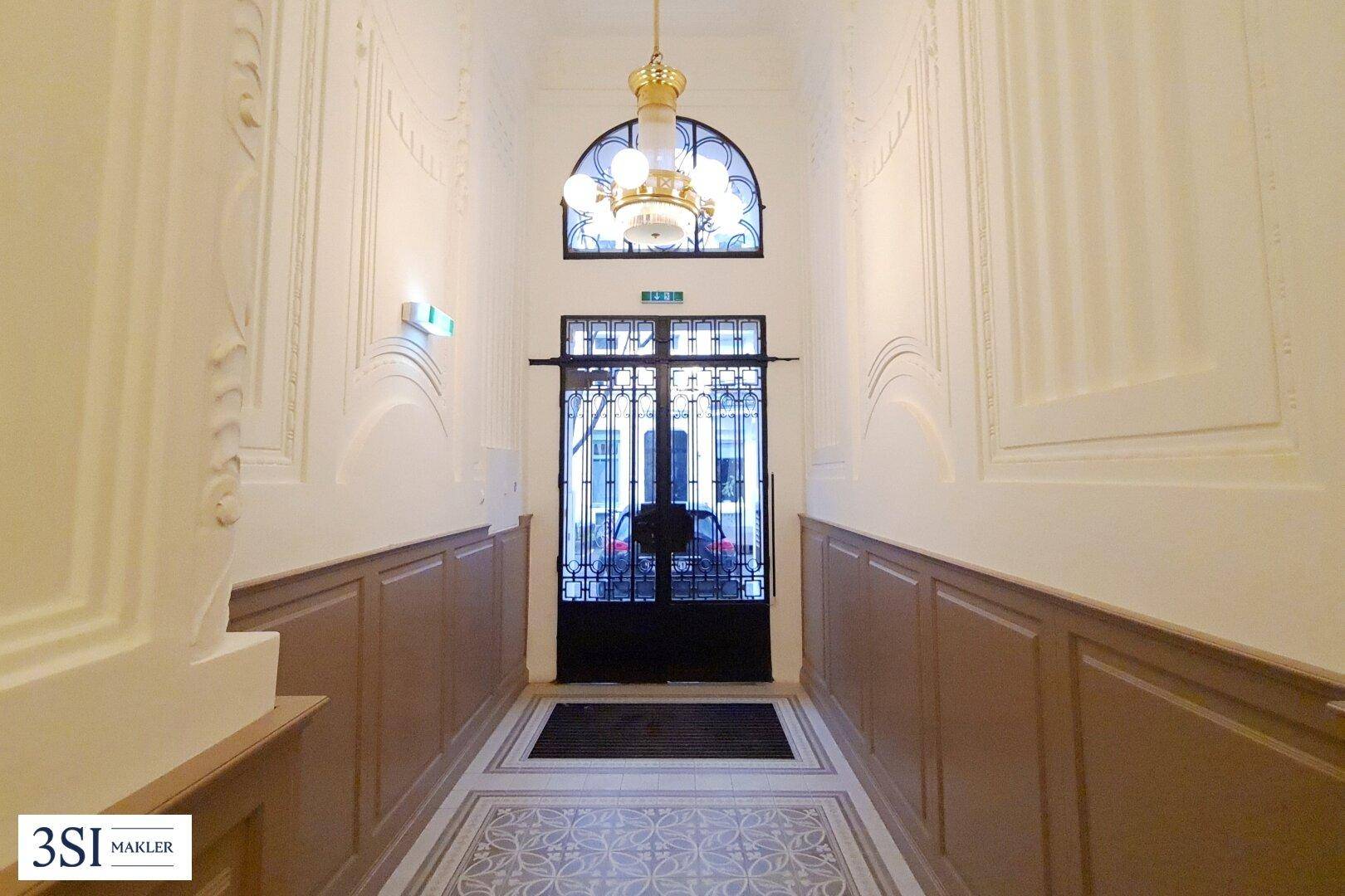 Eleganter Eingangsbereich mit hohen Decken, Stuckverzierungen und einem dekorativen Kronleuchter.