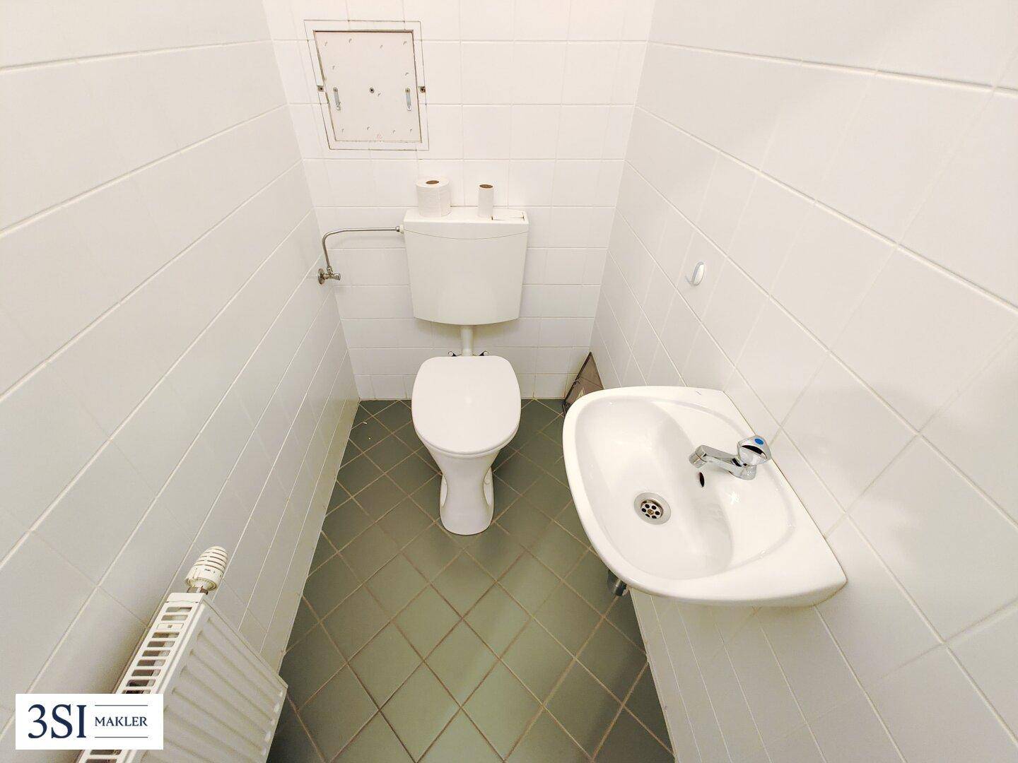 Kleines Gäste-WC mit weißen Fliesen, Toilette und Handwaschbecken.