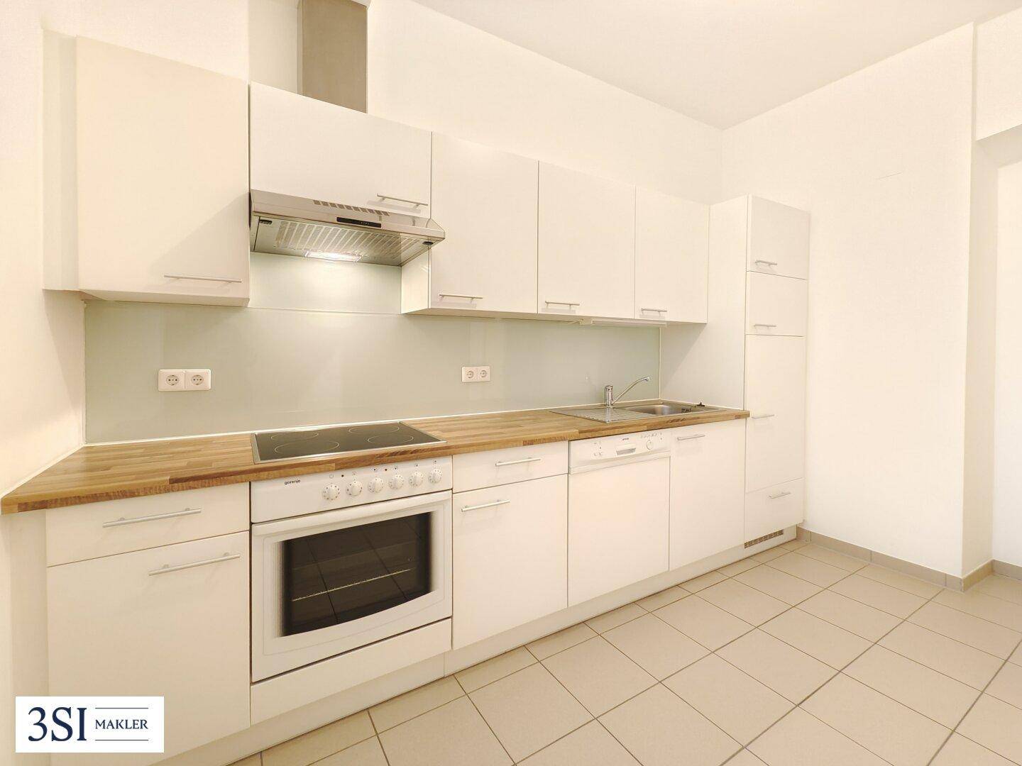 Moderne Einbauküche mit weißen Schränken, Holz-Arbeitsplatte und integrierten Geräten.