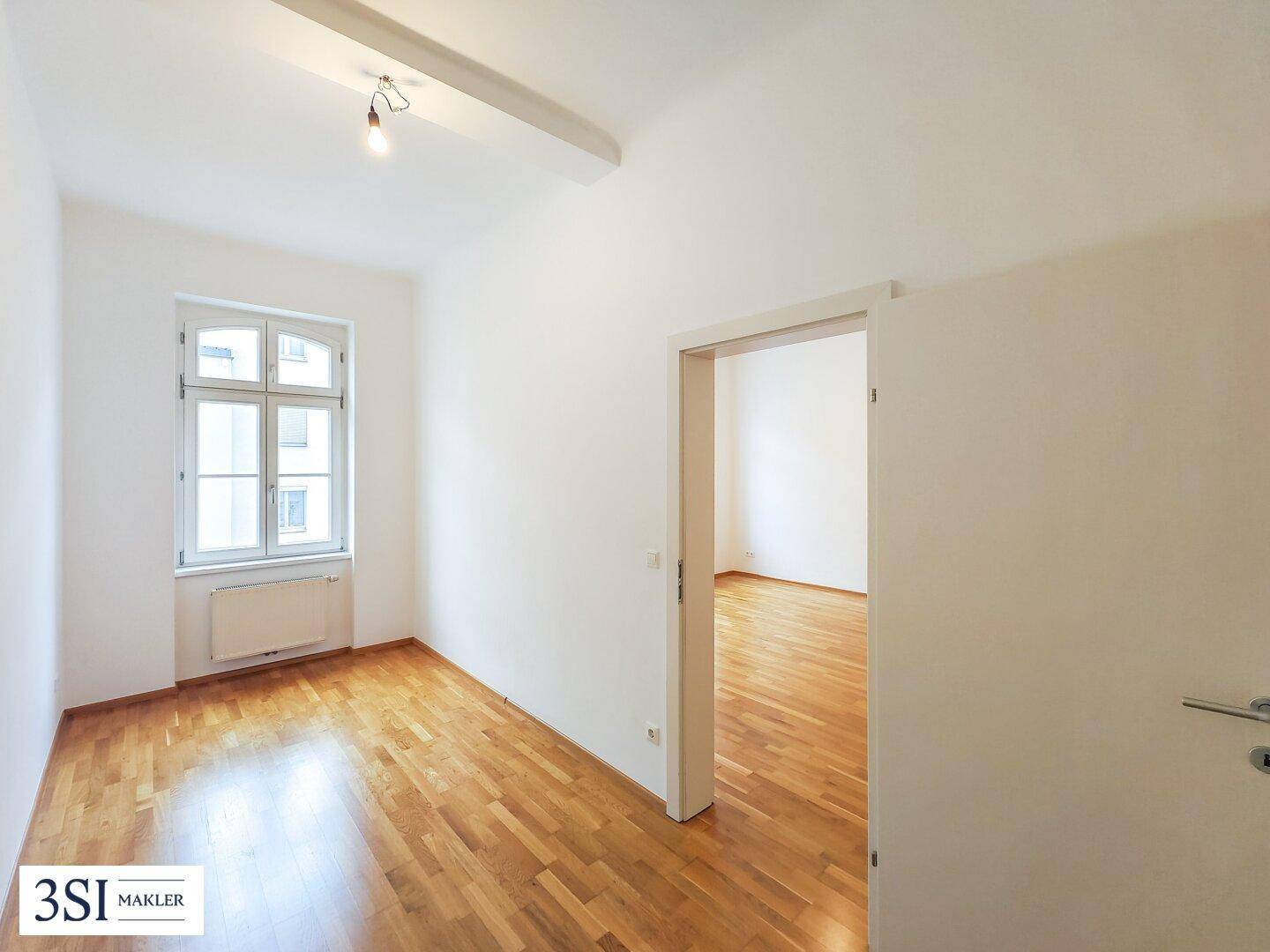 Lichtdurchfluteter Raum mit Parkettboden und einem großen Fenster.