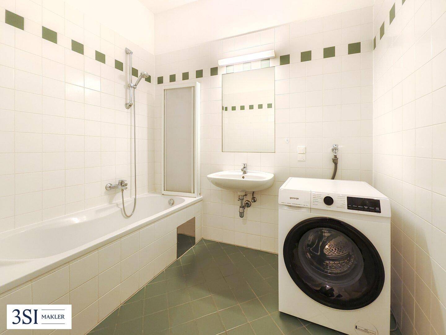 Badezimmer mit Badewanne, Dusche, Waschbecken und Waschmaschine, gefliest in Weiß und Grün.