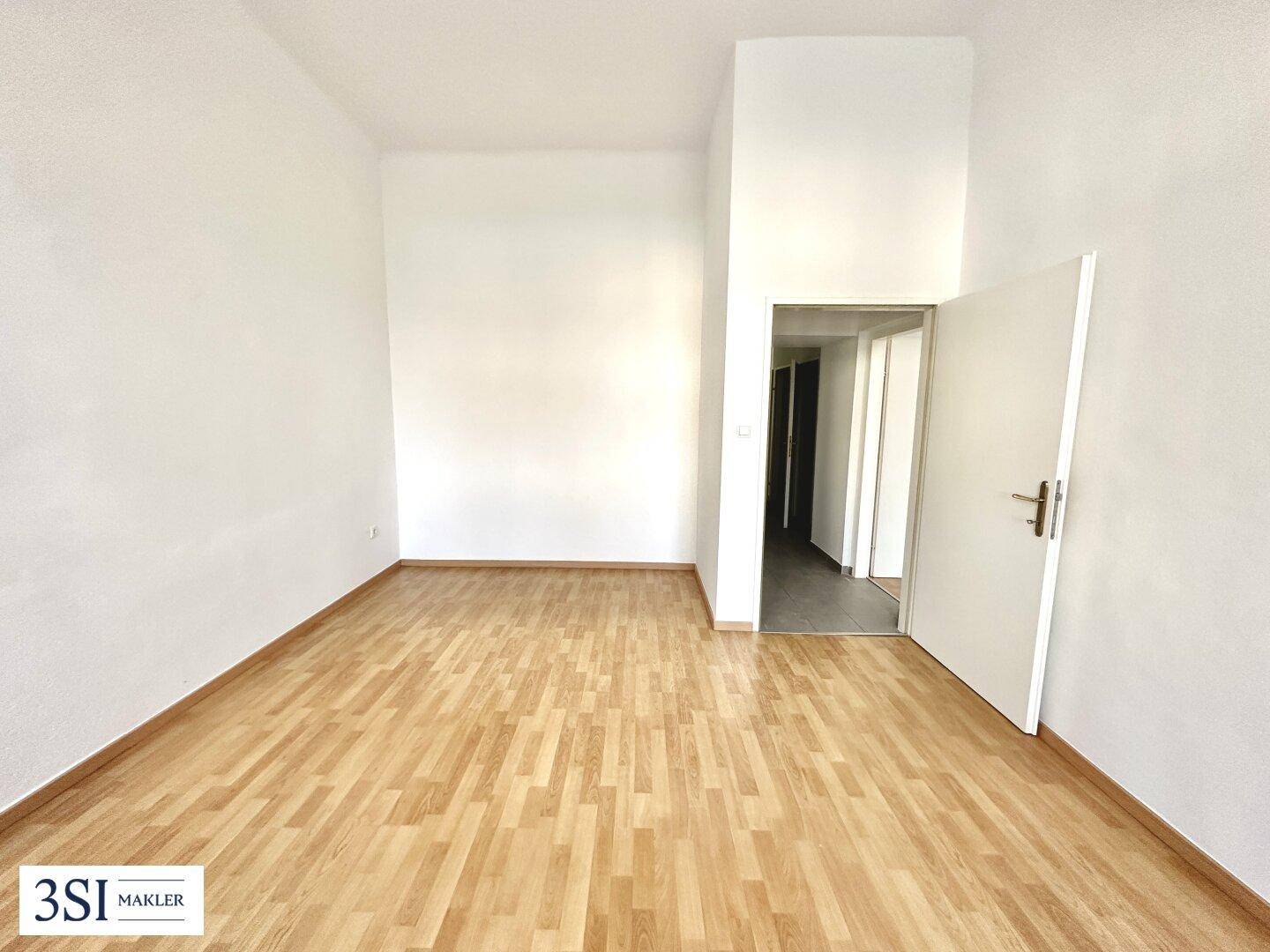 Heller, leerer Raum mit weiß gestrichenen Wänden und warmem Holzparkettboden.