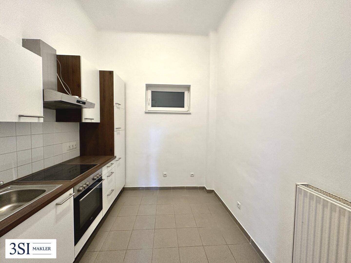Funktionale Einbauküche mit weißen Schränken, dunkler Arbeitsplatte und Fliesenboden, inklusive Fenster.