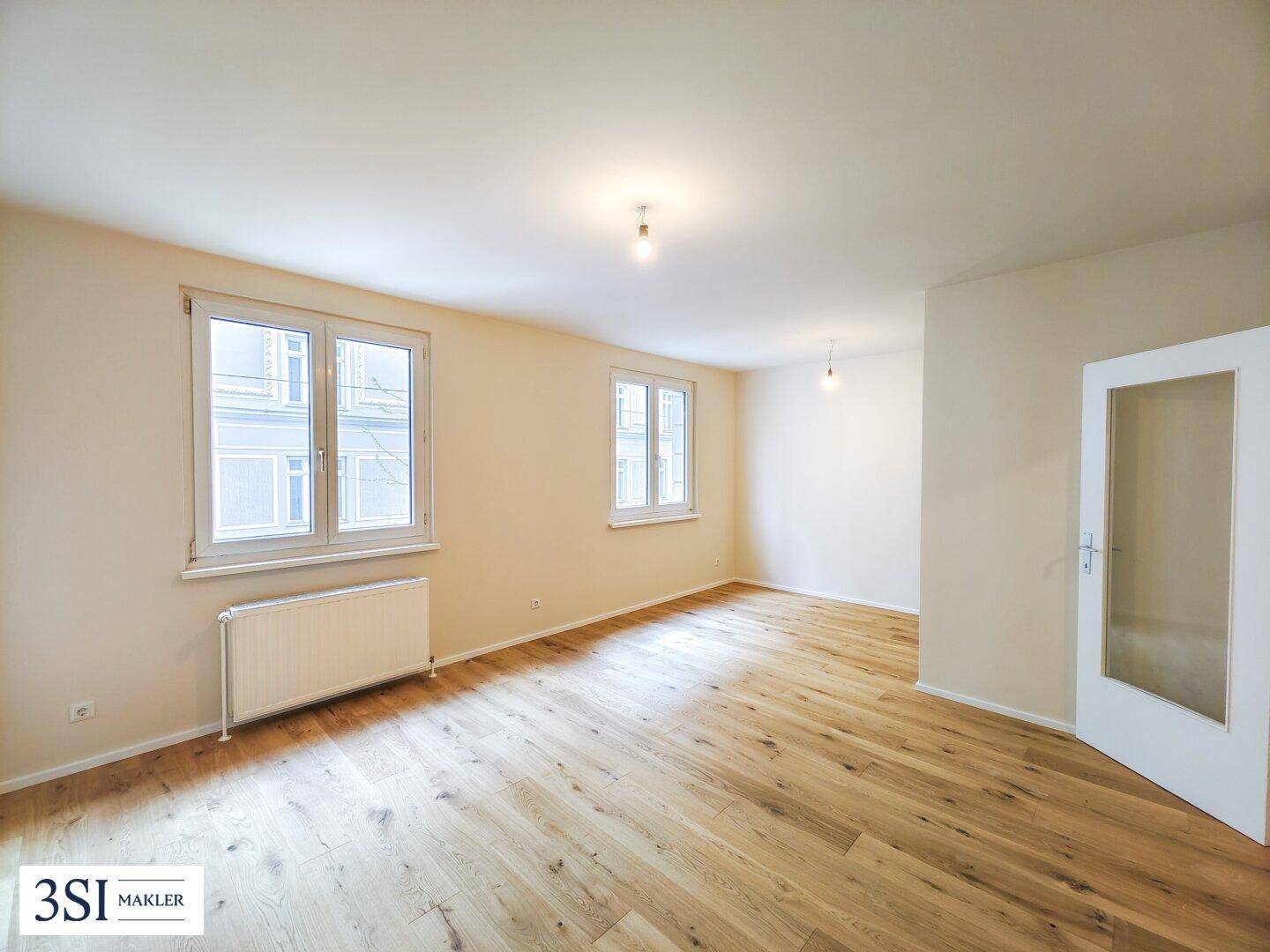 Heller, leerer Raum mit Holzboden und zwei großen Fenstern, ideal als Schlaf- oder Wohnzimmer.