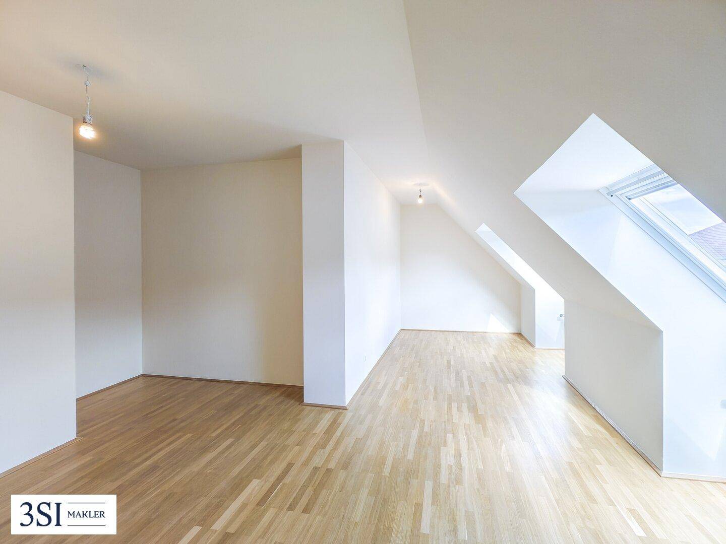 Heller Dachgeschossraum mit schrägen Wänden, Holzboden und einem großen Dachfenster für viel Licht.