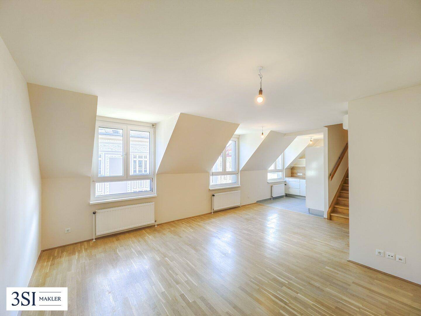 Geräumiger Dachgeschosswohnraum mit schrägen Decken, Holzboden und viel Tageslicht durch mehrere Fenster.
