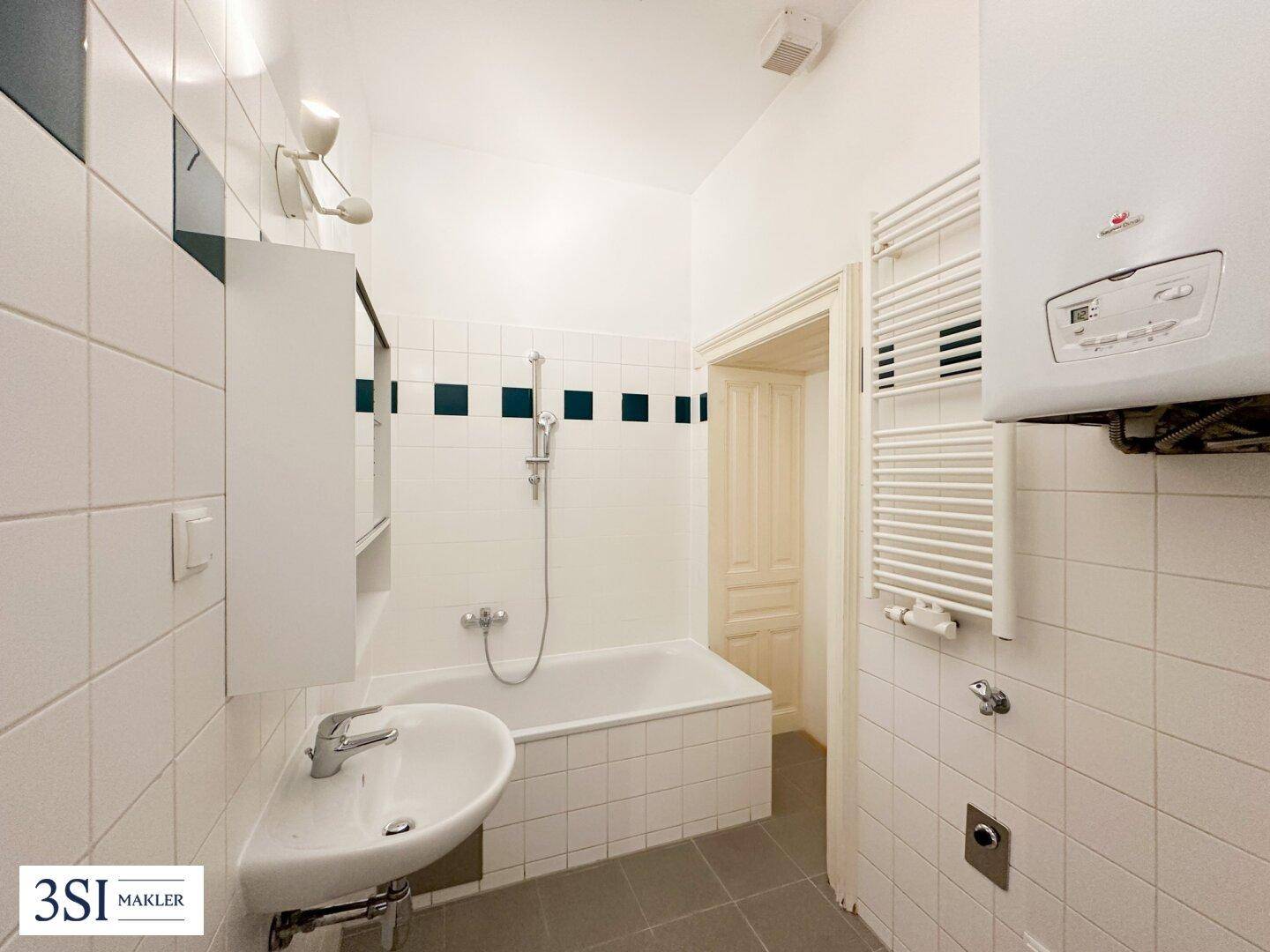 Badezimmer mit Badewanne, Waschbecken und Wandfliesen in Weiß mit grünen Akzenten.