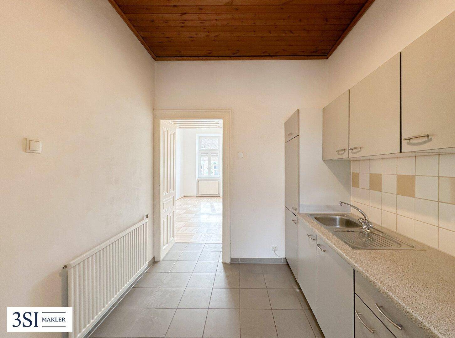 Küchenbereich mit Fliesenboden, Holzdecke und Blick in ein angrenzendes Zimmer.