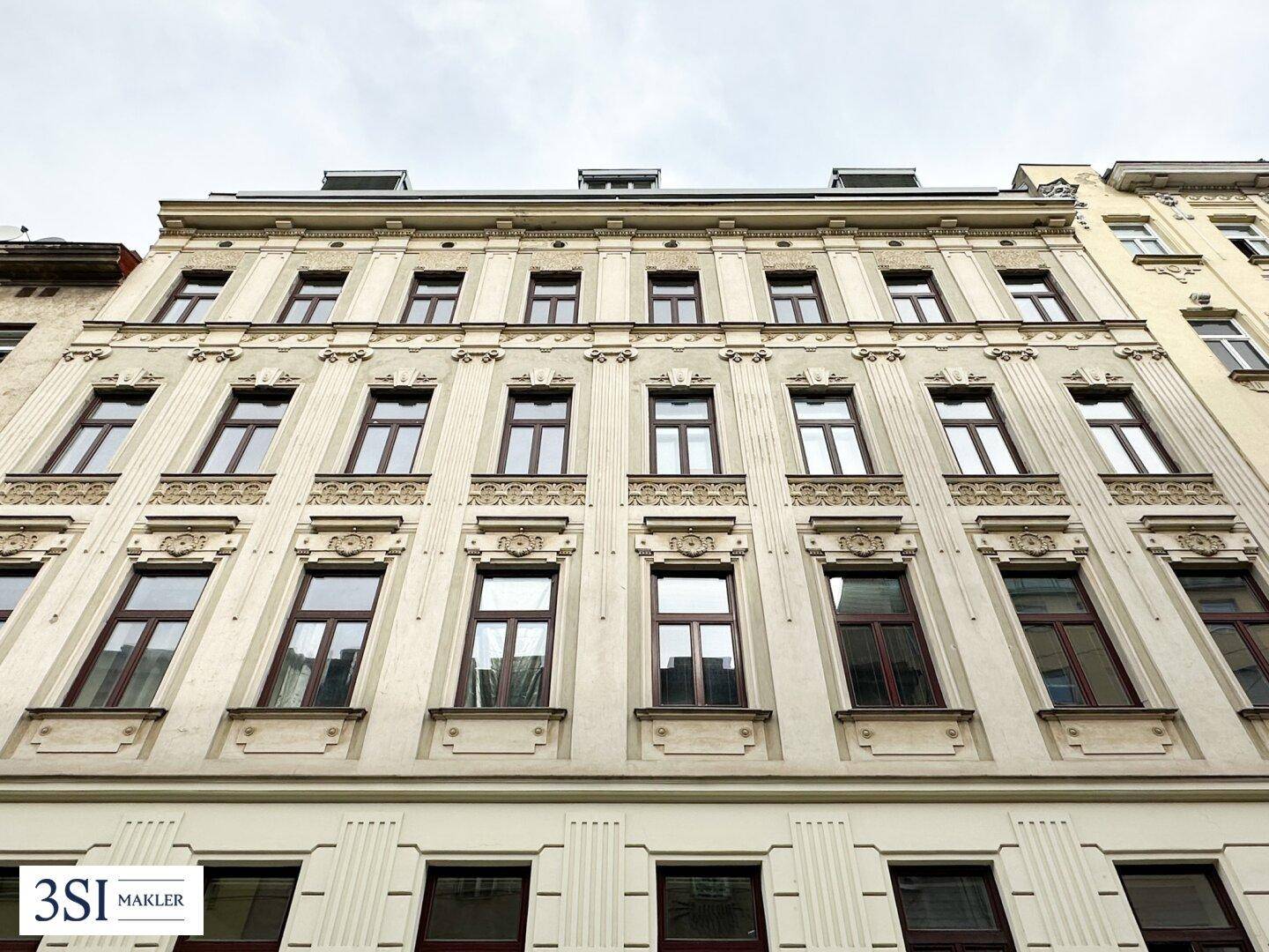 Historisches Mehrfamilienhaus mit reich verzierter Stuckfassade und großen Fenstern in städtischer Umgebung.
