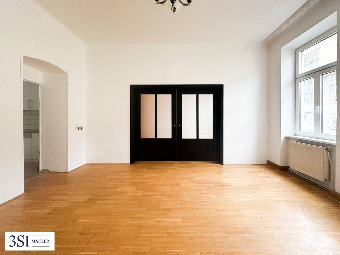 Geräumiger Wohnbereich mit Parkettboden, hohen Decken und eleganten Doppeltüren.