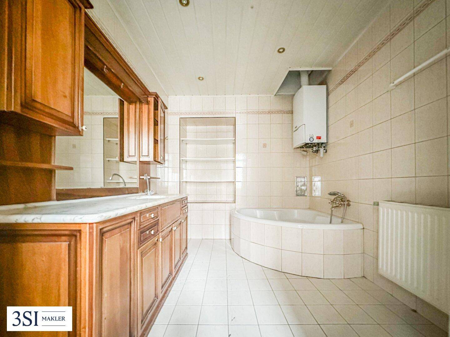 Gefliestes Badezimmer mit Eckbadewanne, Holzwaschtisch und Gastherme an der Wand.