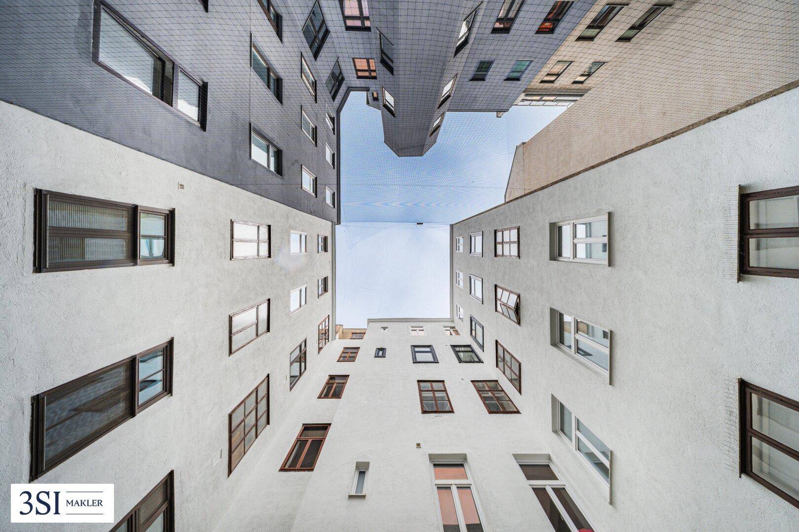 Blick nach oben in einen Innenhof, umgeben von verschiedenen Gebäudefassaden mit unterschiedlichen architektonischen Stilen.