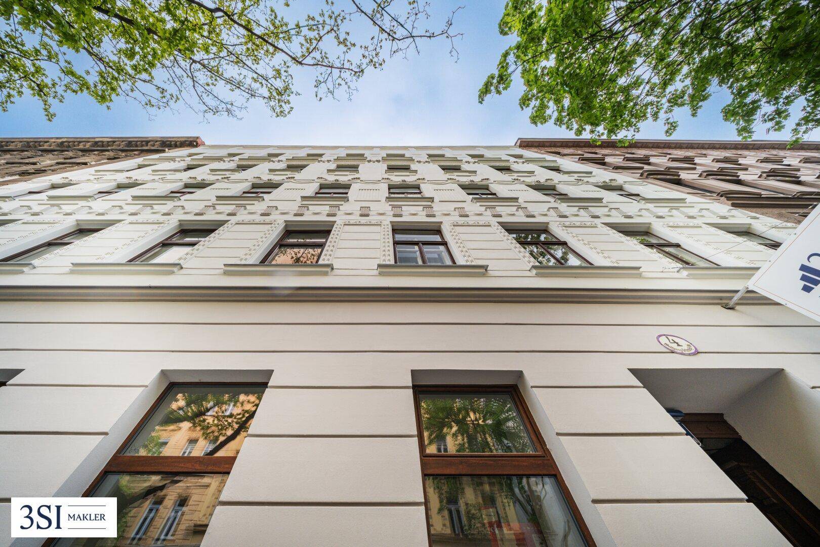 Detailansicht der weißen Altbau-Fassade mit vielen Fenstern und dekorativen Elementen, von unten nach oben fotografiert.