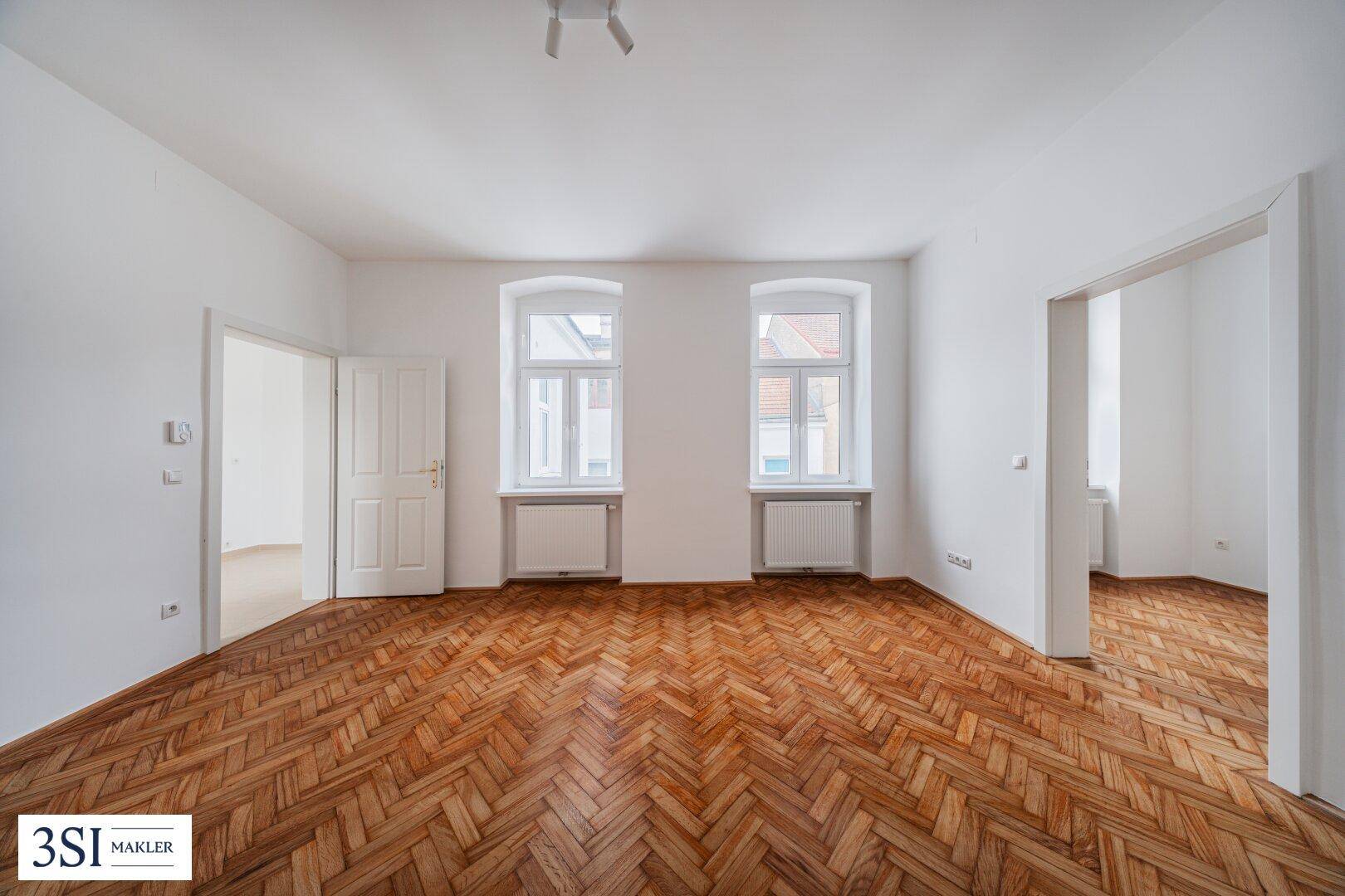 Helles, leeres Zimmer mit Fischgrätparkettboden und zwei Fenstern, bereit zur individuellen Gestaltung.