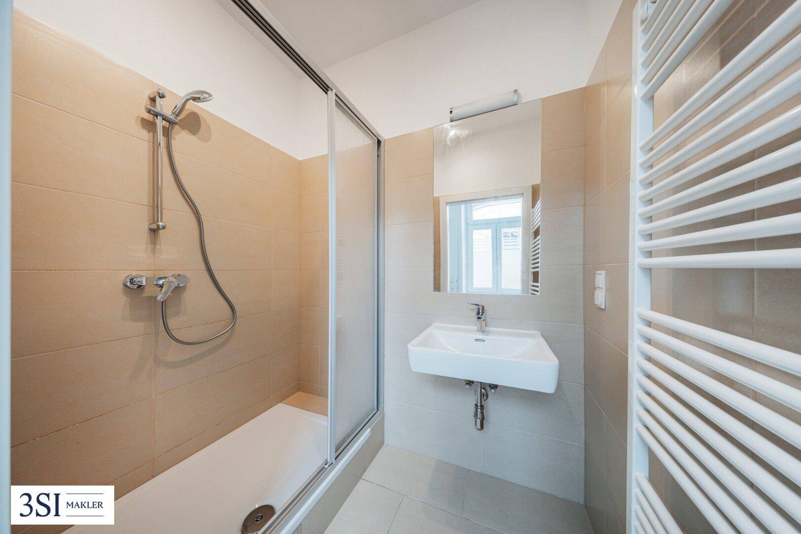Modernes Badezimmer mit Duschkabine, Waschbecken und beheiztem Handtuchhalter in hellen Farbtönen.