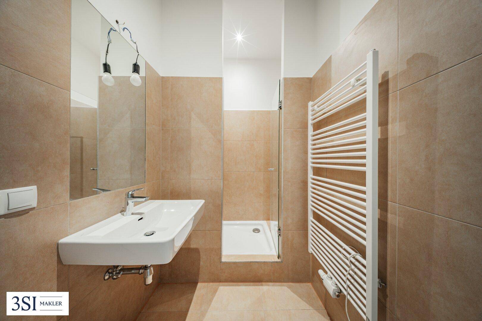 Modernes Badezimmer mit beigefarbenen Fliesen, einer Dusche, einem einzelnen Waschbecken und beheiztem Handtuchhalter.
