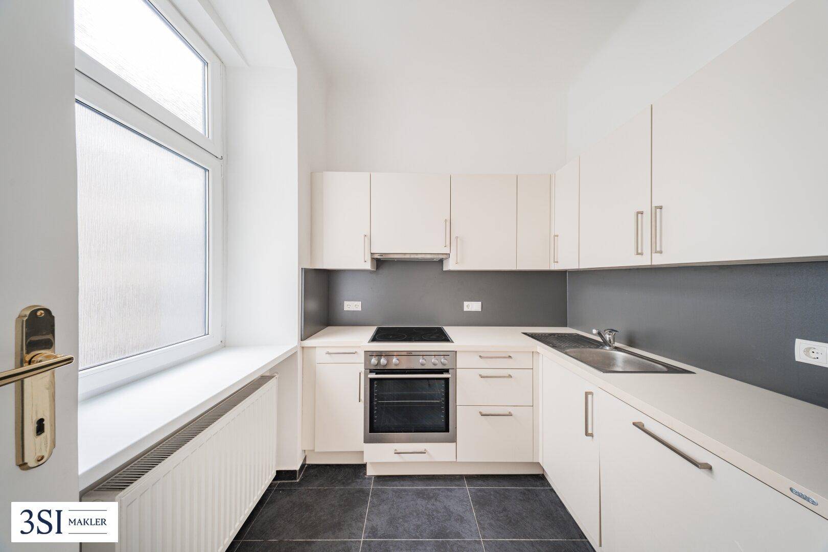 Funktionale Küche mit weißen Schränken, dunklem Fliesenspiegel, integriertem Backofen und Dunstabzugshaube.
