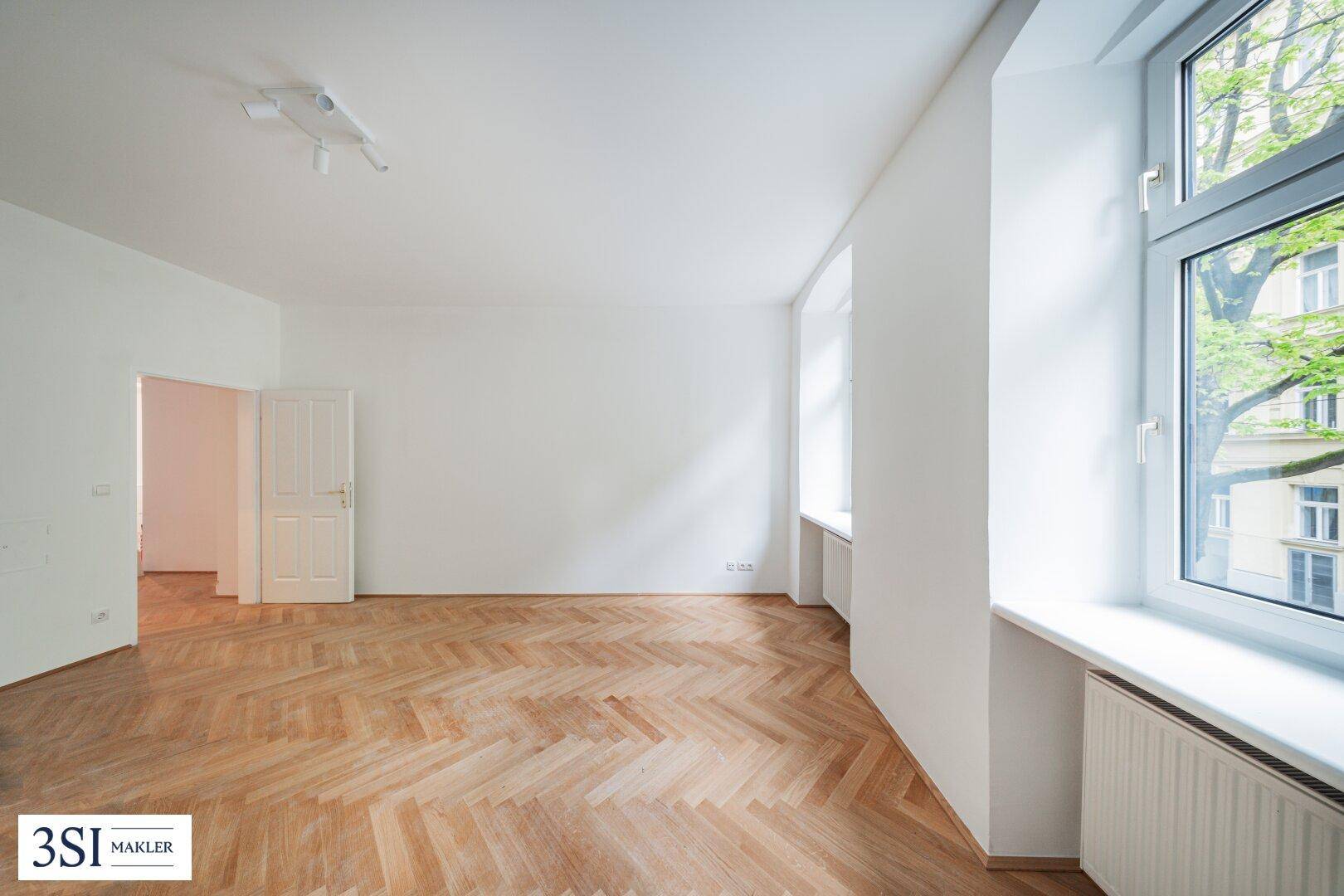 Großes, lichtdurchflutetes Wohnzimmer mit Fischgrätparkett und hohen Fenstern.