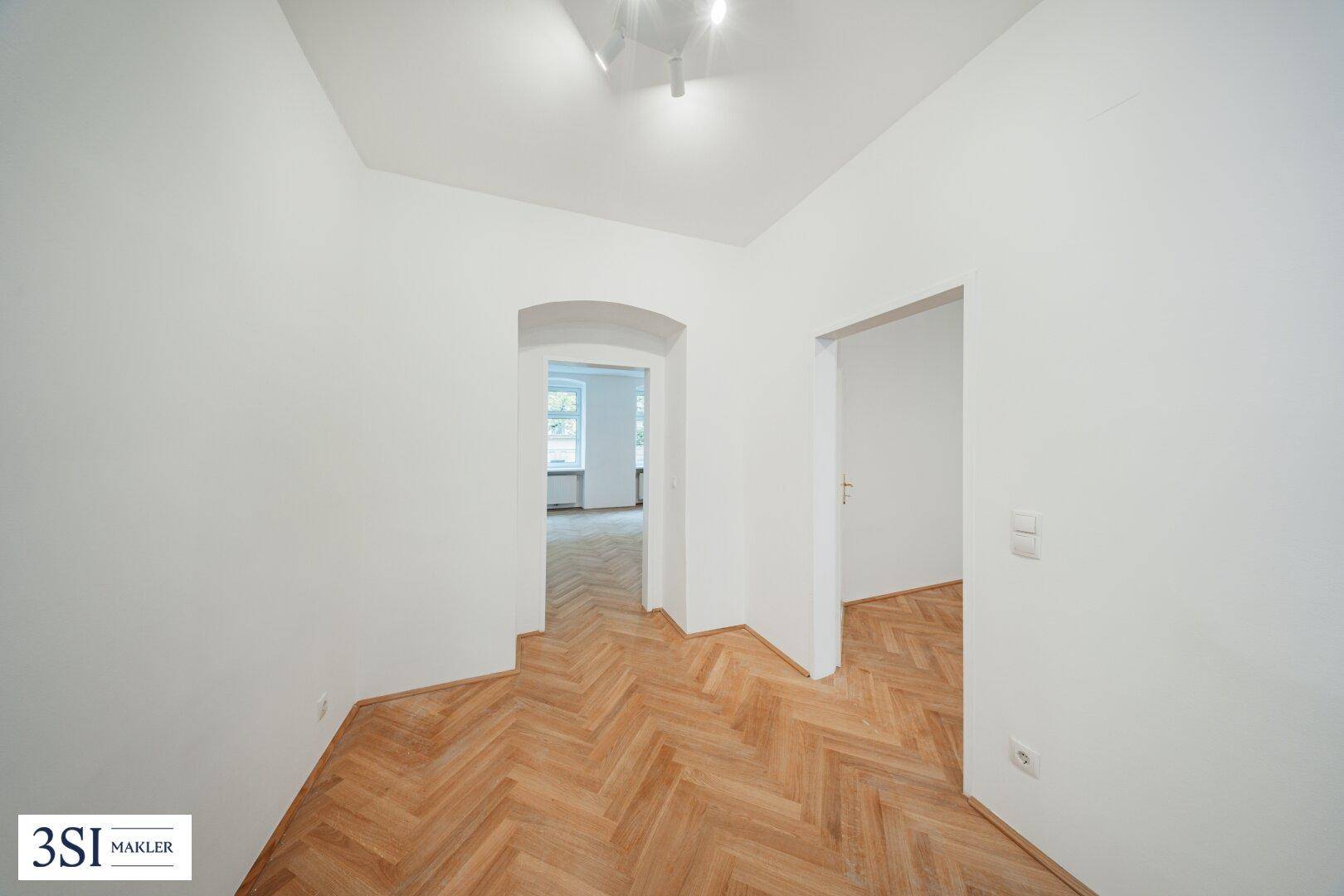 Flur mit Fischgrätparkett und einem eleganten Rundbogen, der zu einem weiteren Zimmer führt.