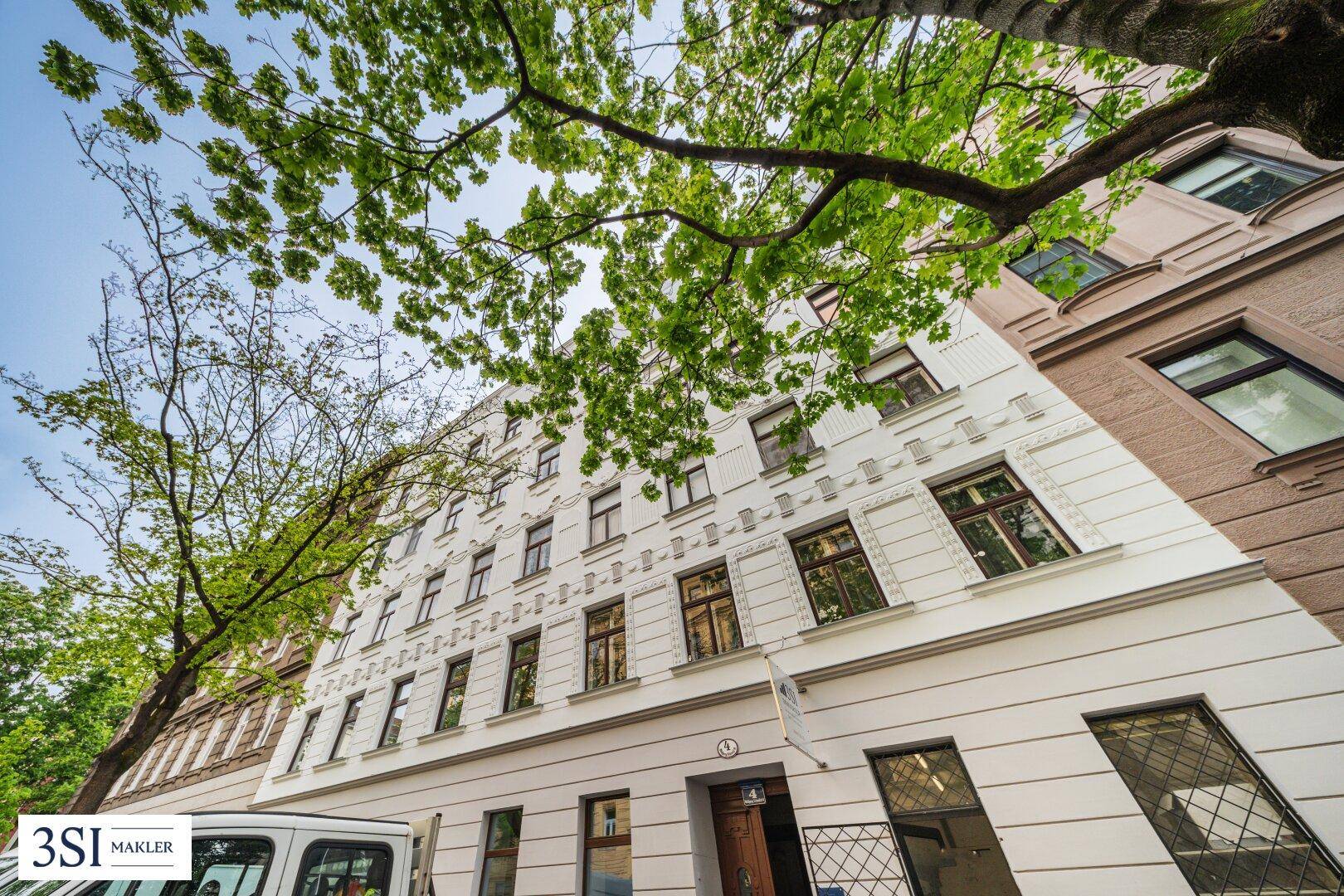 Historisches Mehrfamilienhaus mit klassischer Fassade und vielen Fenstern, umgeben von Bäumen.