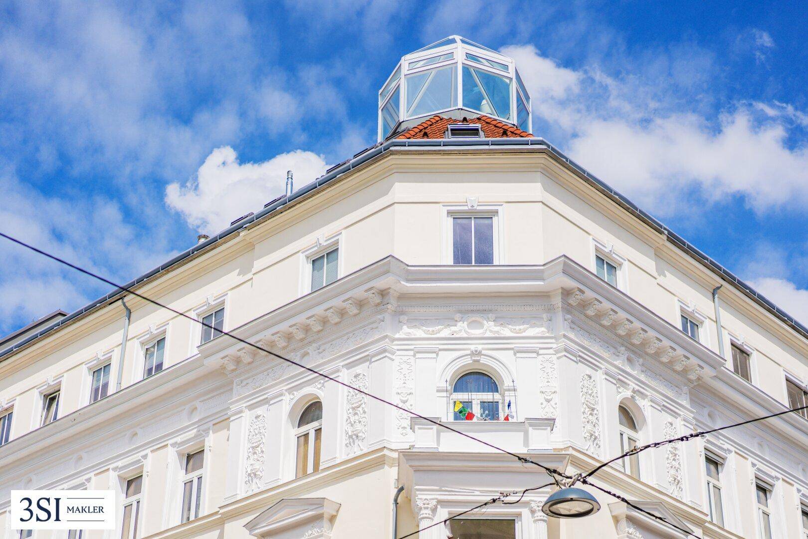 Detailansicht der oberen Etagen eines historischen Gebäudes mit einem modernen Glasdachaufbau.