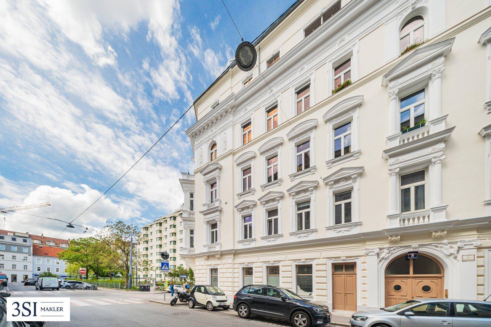 Elegante Fassade eines Altbaus mit großen Fenstern und klassischem Eingangsbereich in urbaner Umgebung.
