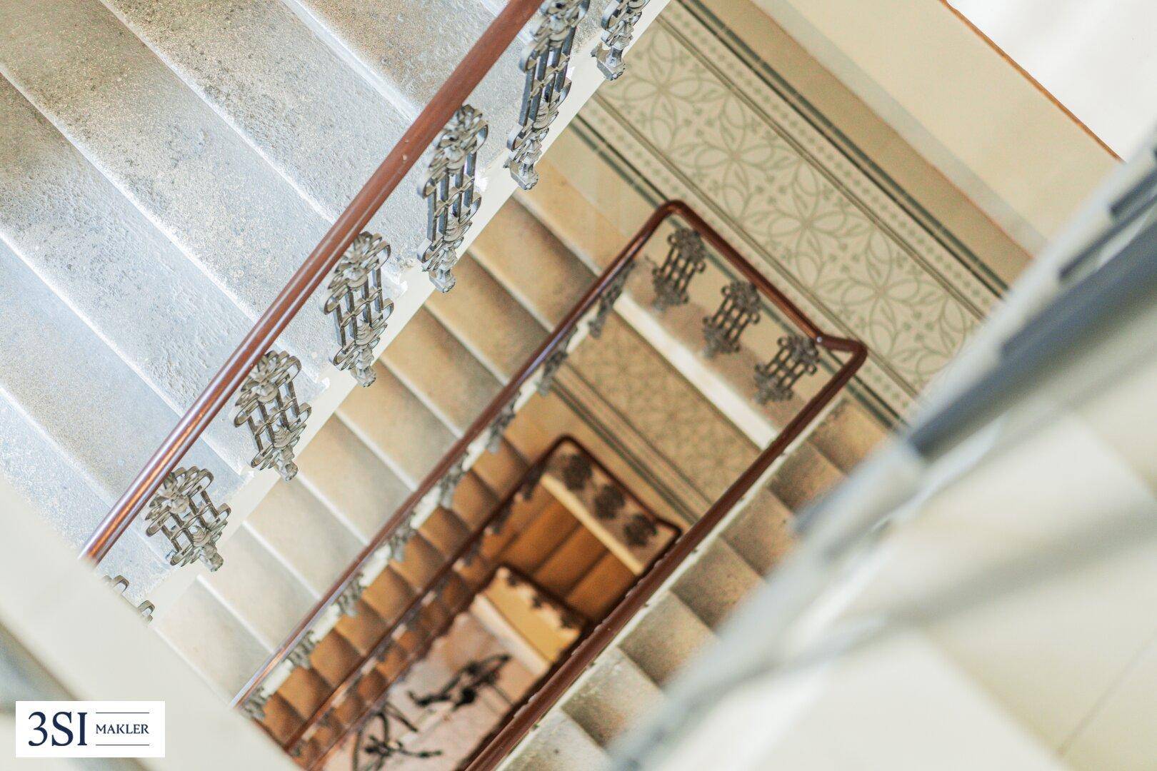 Elegantes Treppenhaus mit kunstvollen Geländern, Steinstufen und gemusterten Teppichläufern.