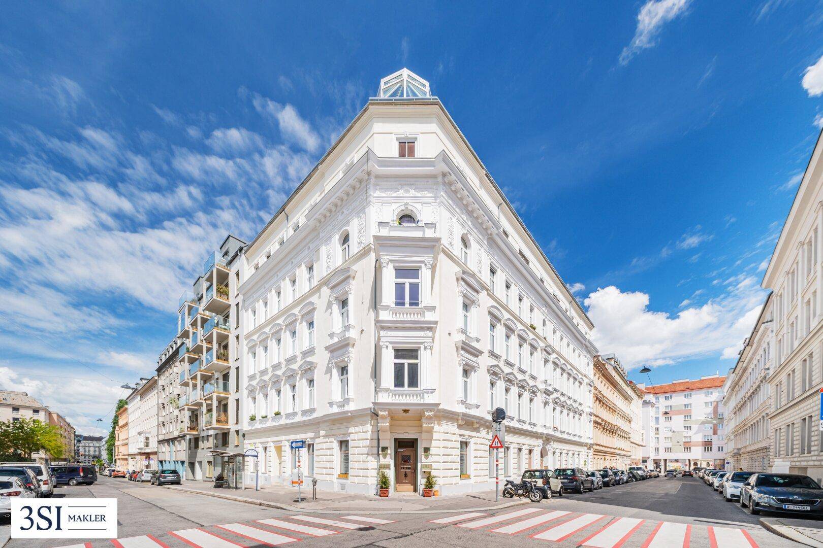 Prächtiges Eckgebäude in urbaner Umgebung mit historischer Architektur und blauem Himmel, an einer belebten Straße.