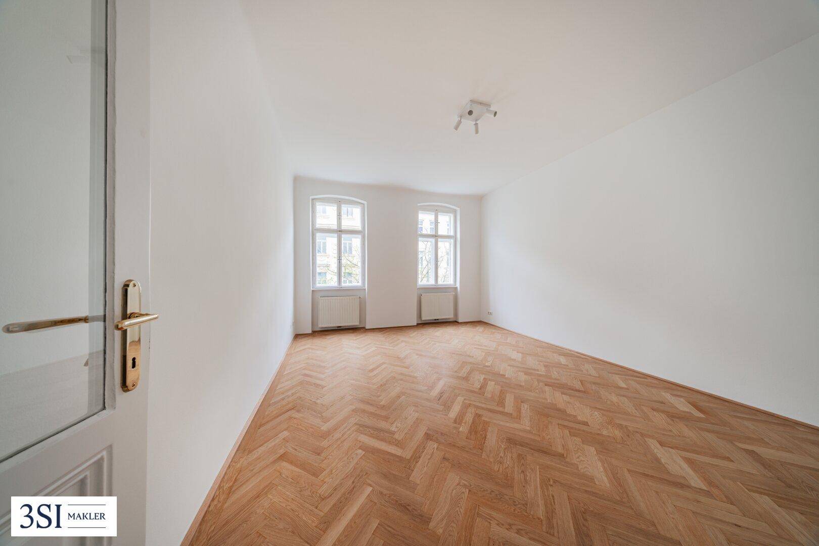 Leerer Raum mit Fischgrätparkett und zwei Fenstern, ideal für Schlaf- oder Wohnbereich, mit viel Tageslicht.