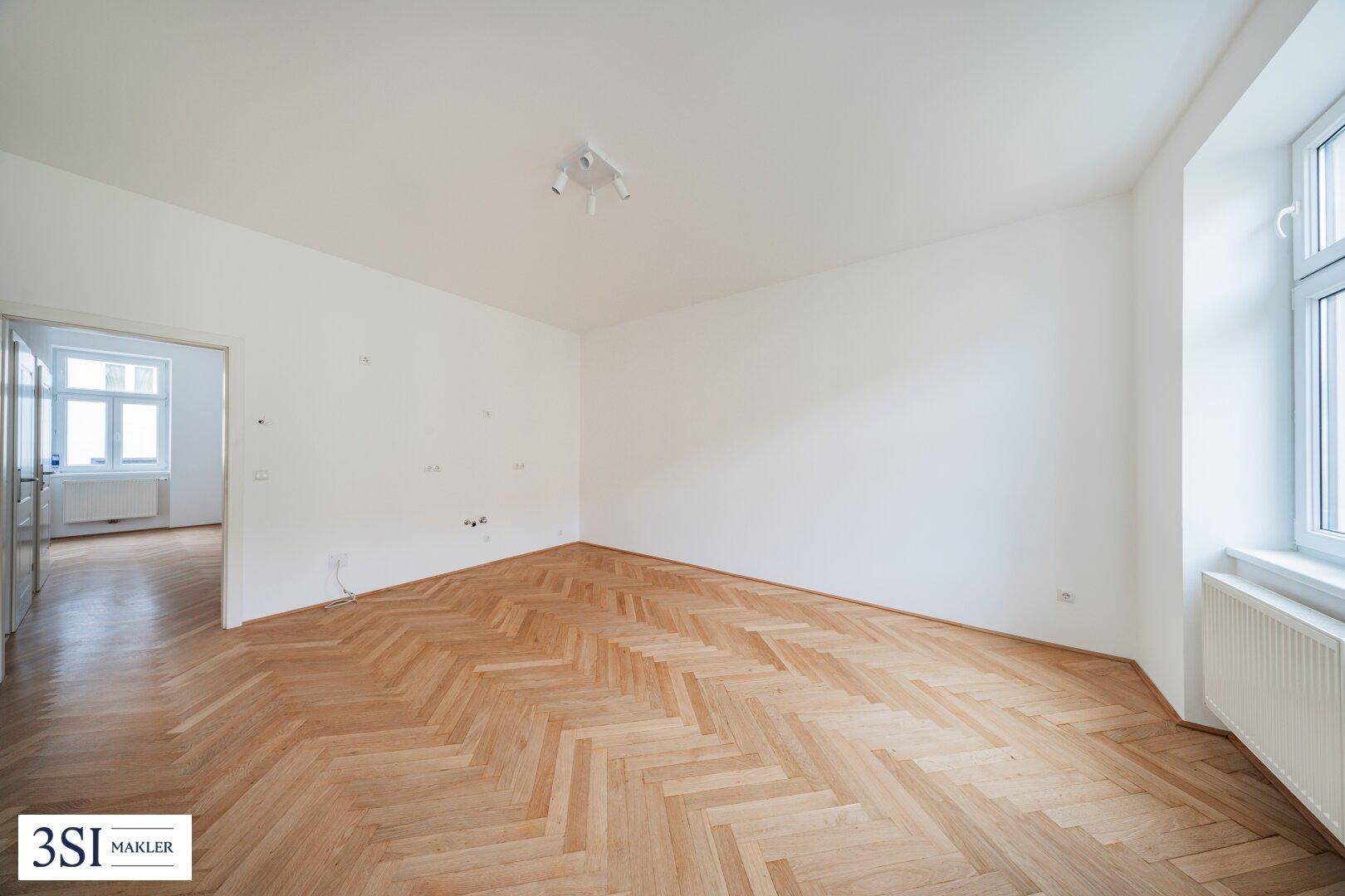 Heller Raum mit Fischgrätparkett und weiß gestrichenen Wänden, bereit zur Einrichtung und mit guter Beleuchtung.