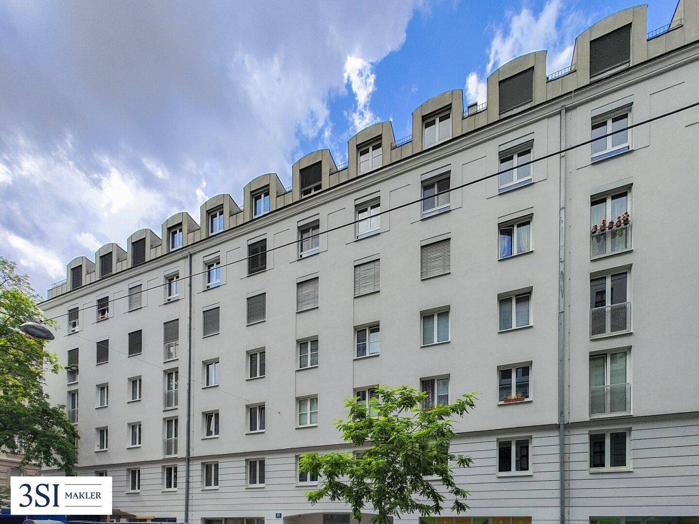 Fassade eines modernen Wohngebäudes mit zahlreichen Fenstern, Rollläden und markanter Dachkonstruktion.
