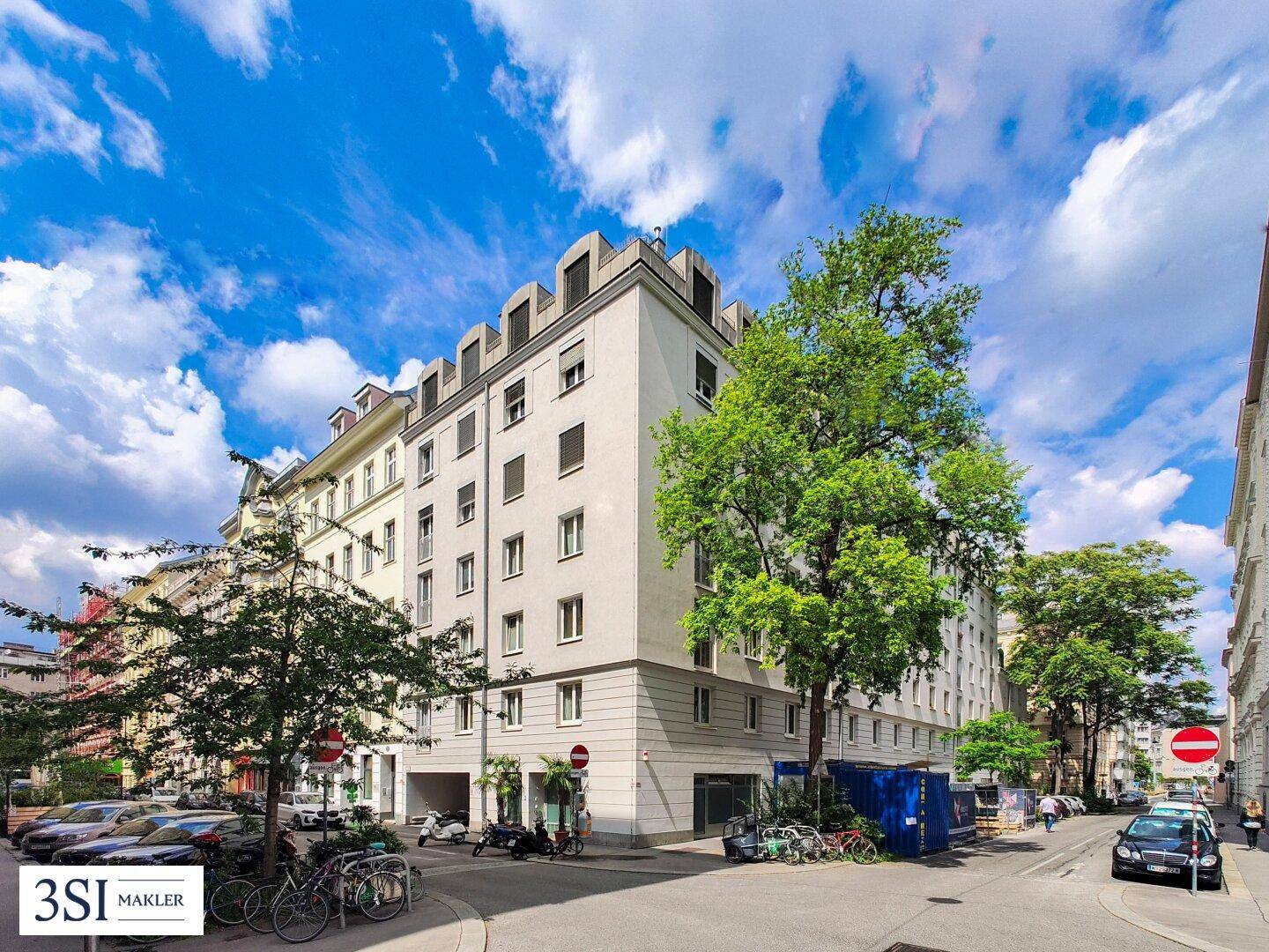 Mehrstöckiges Wohngebäude mit klassischer Fassade und Bäumen an einer städtischen Straße.