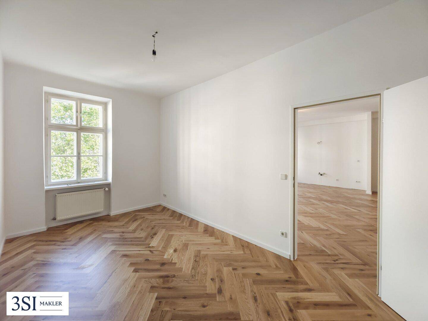 Heller, leerer Raum mit Fischgrätparkett, hohen Decken und großem Fenster, bereit zum Einzug.