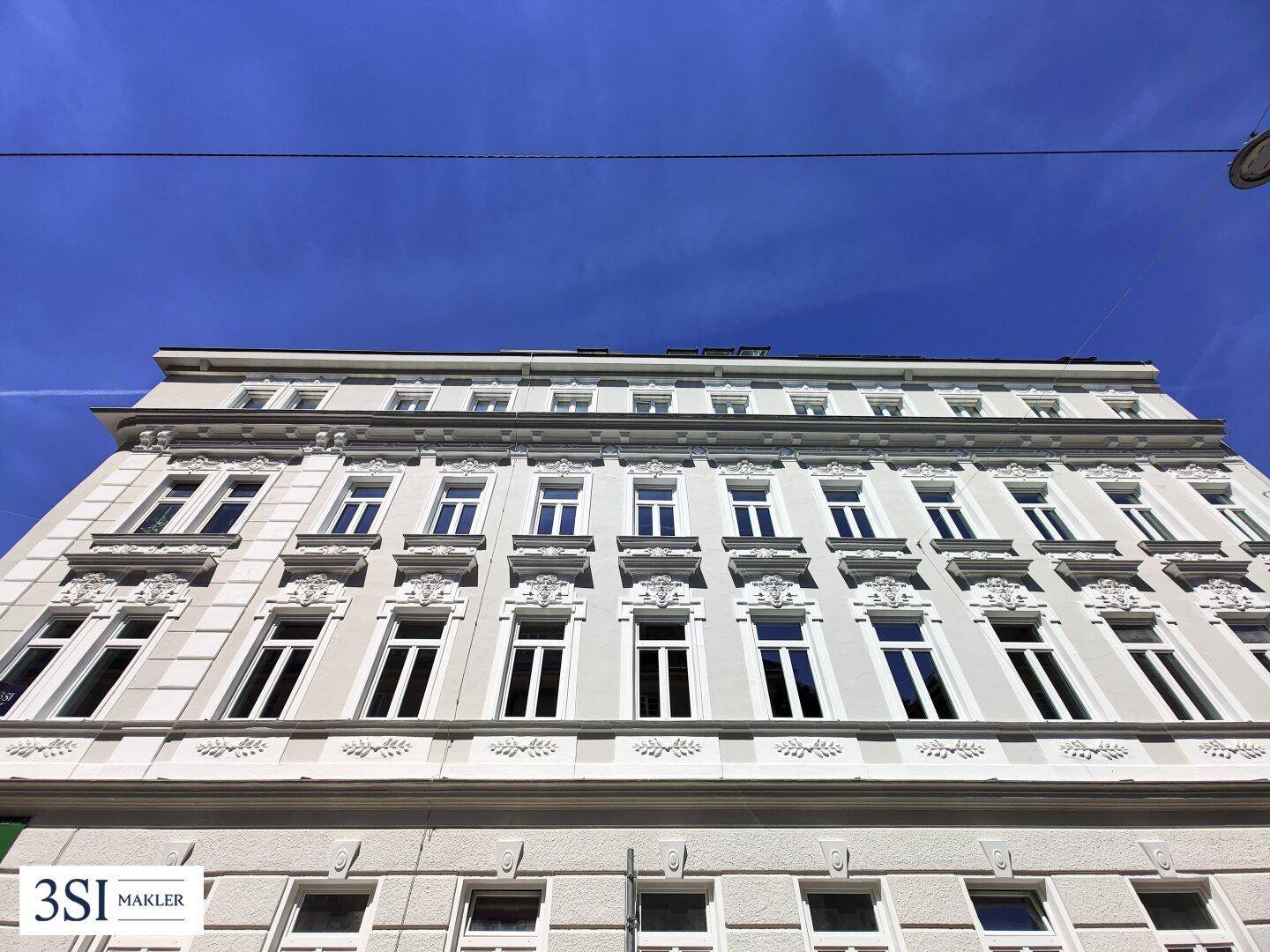 Historische Fassade eines Altbaus mit reich verzierten Fenstern und Stuckelementen unter blauem Himmel.