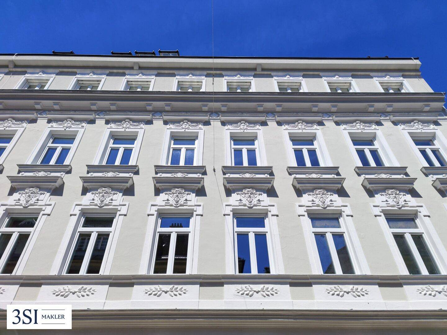 Historische Fassade eines Gebäudes mit reich verzierten Fenstern und Stuckelementen unter blauem Himmel.