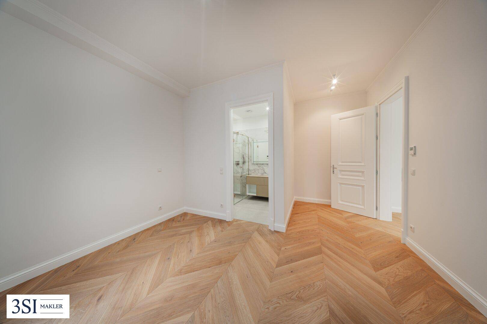 Heller Raum mit Fischgrätparkett und direktem Zugang zu einem modernen Badezimmer.