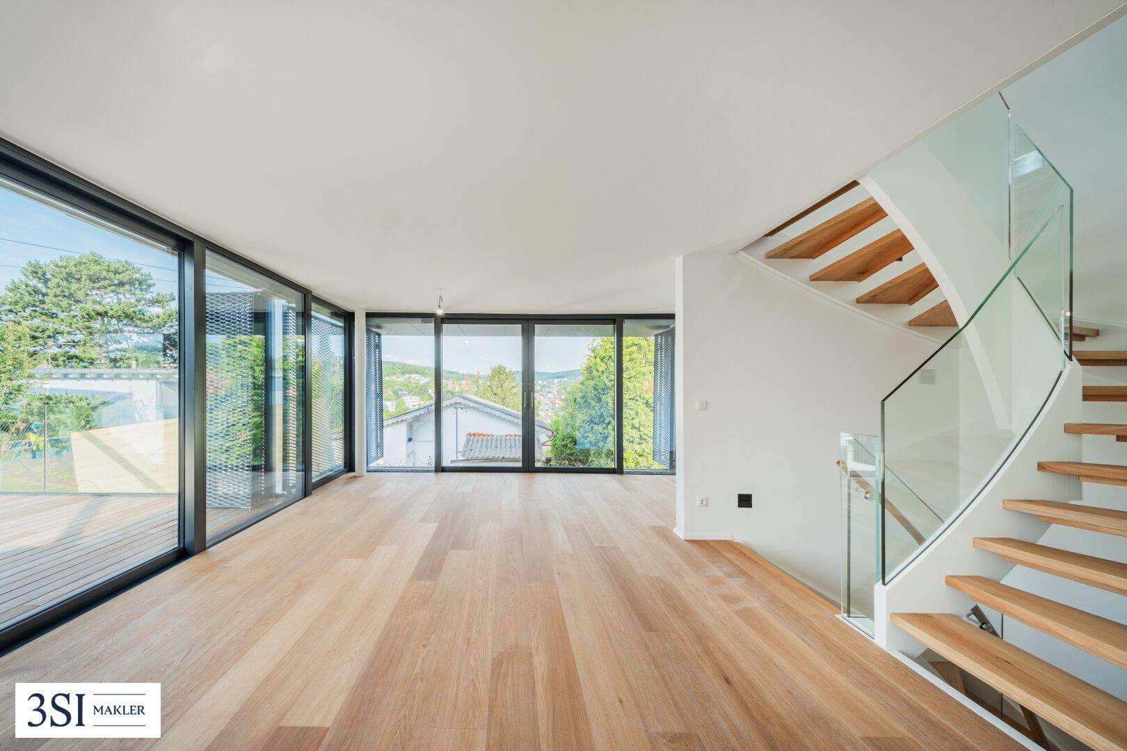 Geräumiger Wohnbereich mit Holzparkett, großen Fenstern und einer modernen Holztreppe mit Glasgeländer.