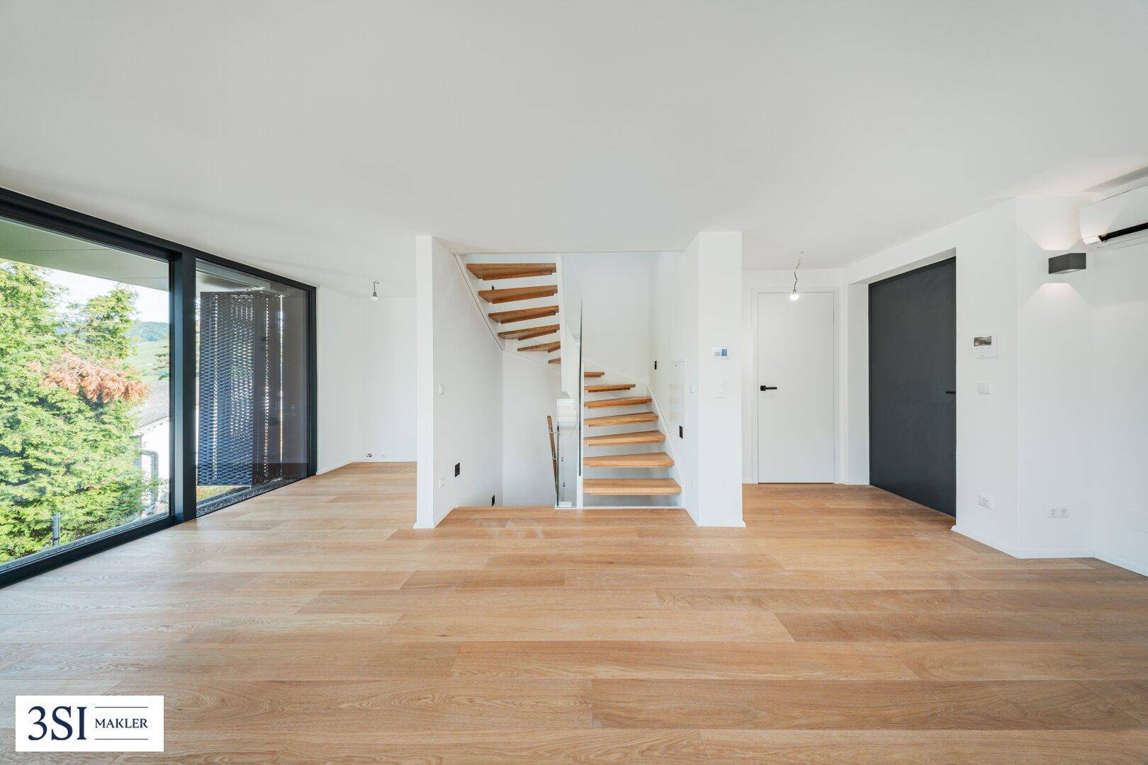 Offener Wohnbereich mit hellem Holzboden, weiß gestrichenen Wänden und einer modernen Treppe.