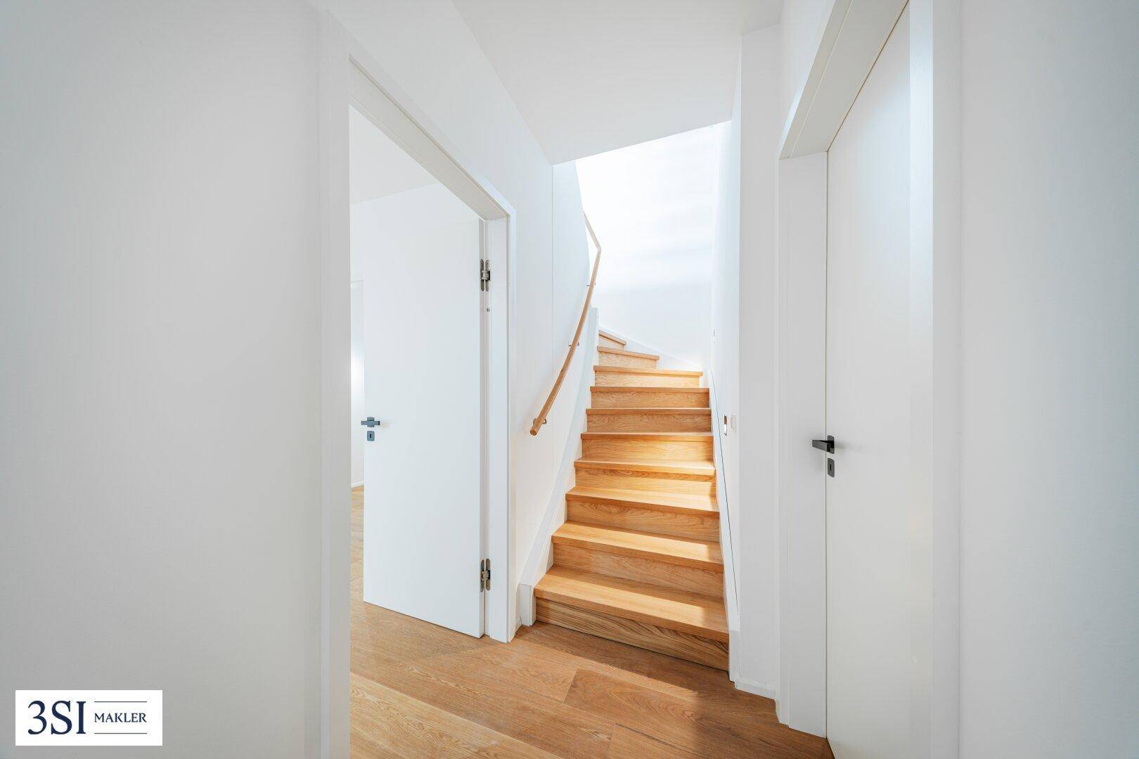 Heller Flur mit Holztreppe und schlichten weißen Türen, die zu weiteren Räumen führen.