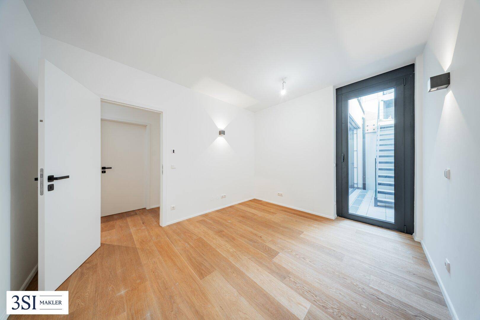 Helles Schlafzimmer mit Holzboden, weißen Wänden und Zugang zu einem kleinen Außenbereich.